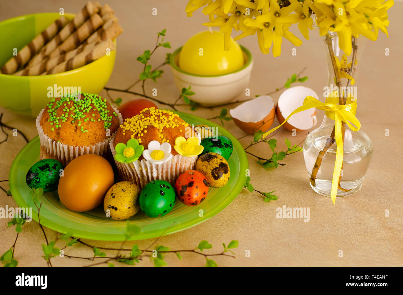 Muffins decorated with sprinkles, flowers of mastic, colored easter quail eggs on a green plateon the kitchen table. Happy Easter holiday and greeting Stock Photo