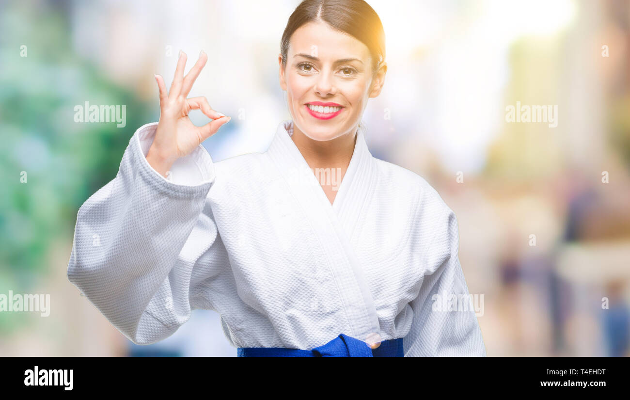 Young beautiful woman wearing karate kimono uniform over isolated background smiling positive doing ok sign with hand and fingers. Successful expressi Stock Photo