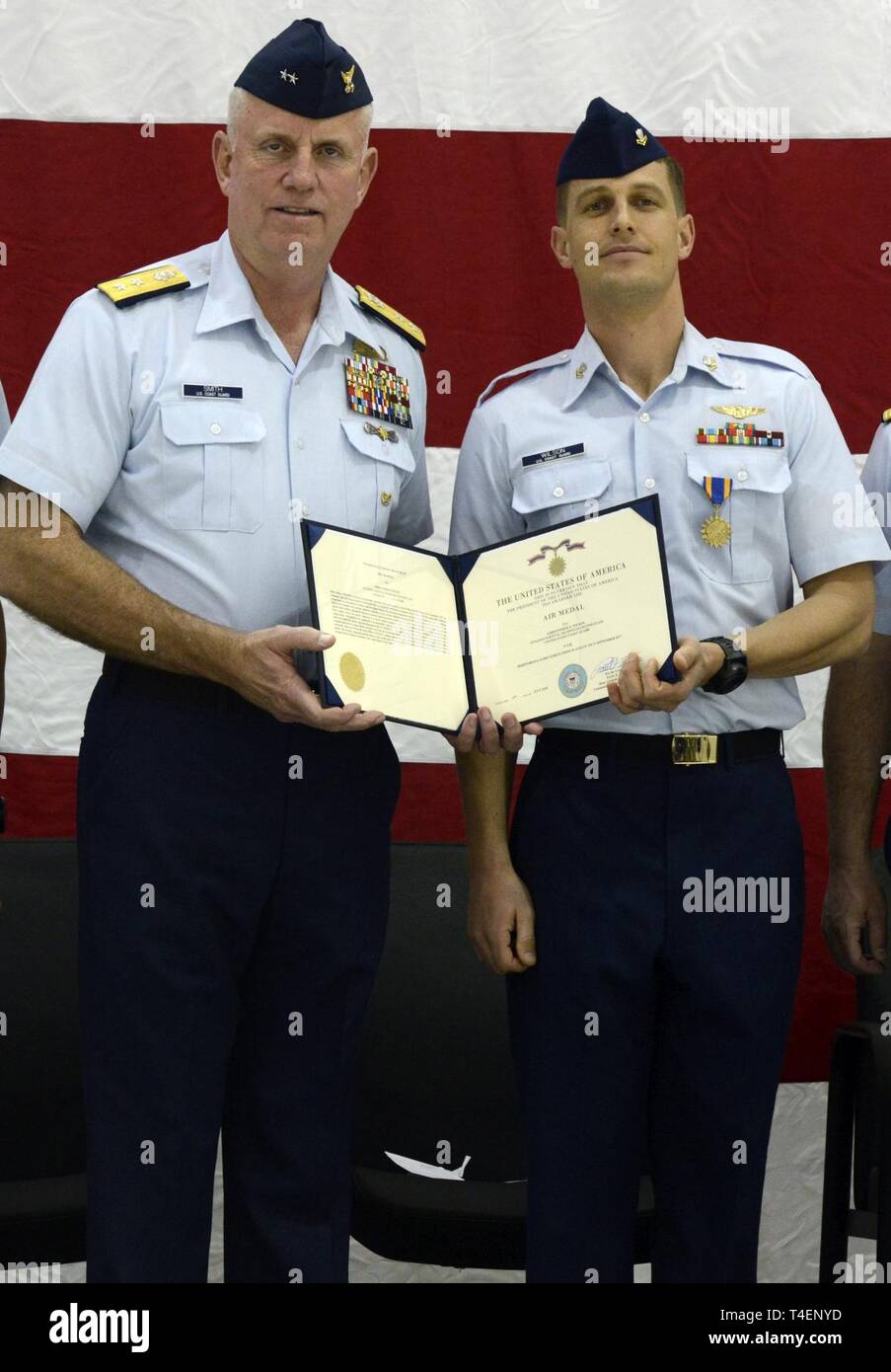 Petty Officer 2nd Class Christopher Wilson (right) displays the Air Medal award citation presented to him by Rear Adm. Keith Smith, commander of the Coast Guard’s 5th District, (left) during an award ceremony at Coast Guard Air Station Atlantic City New Jersey, April 2, 2019.    Wilson was awarded the Air Medal for meritorious achievement in actions taken during his deployment to Hurricane Harvey.    Coast Guard Stock Photo