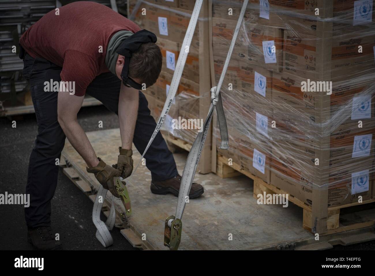 A U.S. military member supporting Combined Joint Task Force-Horn of Africa uses a ratchet strap to secure Plumpy Sup Aid to a pallet in Maputo, Mozambique, April 2, 2019. The task force is helping meet requirements identified by the United States Agency for International Development (USAID) assessment teams and humanitarian organizations working in the region by providing logistics support and manpower to USAID at the request of the Government of the Republic of Mozambique. Stock Photo