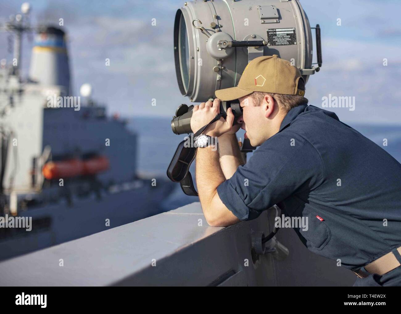 MEDITERRANEAN SEA (April 3, 2019) - Ensign Michael Boehm uses a laser range finder aboard the San Antonio-class amphibious transport dock ship USS Arlington (LPD 24) during a replenishment-at-sea with the Henry Kaiser-class fleet replenishment oiler USNS John Lenthall (T-AO 189), April 3, 2019. Arlington is on a scheduled deployment as part of the Kearsarge Amphibious Ready Group in support of maritime security operations, crisis response and theater security cooperation, while also providing a forward naval presence. Stock Photo