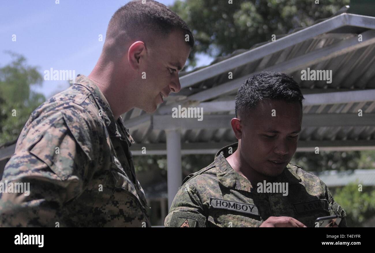 Philippine Army Cpl. Frankie B. Homboy interacts with U.S. Marine Corps Gunnery Sgt. Bradley Ryan Schmidt during a community relations event at Don Eulogio Luistro Elementary School, Batangas, Philippines, during Exercise Balikatan, April 6, 2019. In its 35th iteration, Balikatan is a U.S.-Philippine military training exercise that incorporates humanitarian and civic assistance projects, combined-arms and counter-terrorism training and other events. Homboy, a rifleman with 1st Infantry Battalion Scout Platoon, Philippine Army, is a native of Catarman Northern Samar, Philippines. Schmidt, a nat Stock Photo