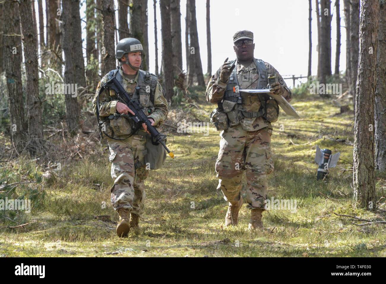 U.S. Army Maj. William Kirby, left, assigned to 2nd Cavalry Regiment, moves to his next objective after identifying a simulated unexploded ordnance while testing for the Expert Field Medical Badge at the 7th Army Training Command’s Grafenwoehr Training Area, Germany, March 29, 2019. To qualify for the badge, Soldiers from U.S. Army Europe, NATO, and other allied and partner nations must complete events such as land navigation, weapons function checks, written tests, medical treatments and evacuations, and a 12 mile ruck march. Stock Photo
