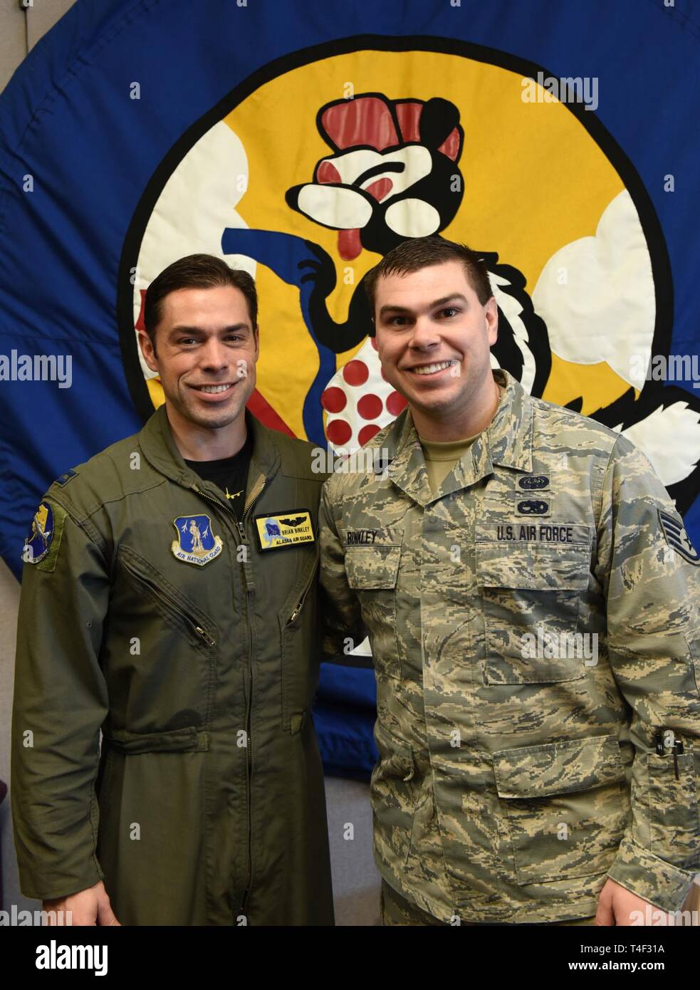 Alaska Air National Guardsmen Capt. Brian Binkley, 168th Air Refueling Squadron pilot, and Staff Sgt. Aaron Binkley, 168th Operations Support Squadron combat crew communications technician, pose in front of the operations group squadron patch on April 7, 2019. The brothers work for the same squadron carrying out different jobs to support the 168th Wing’s air refueling mission. The squadron patch pictures a skunk holding a gas nozzle in the sky to illustrate “passing gas.” Stock Photo