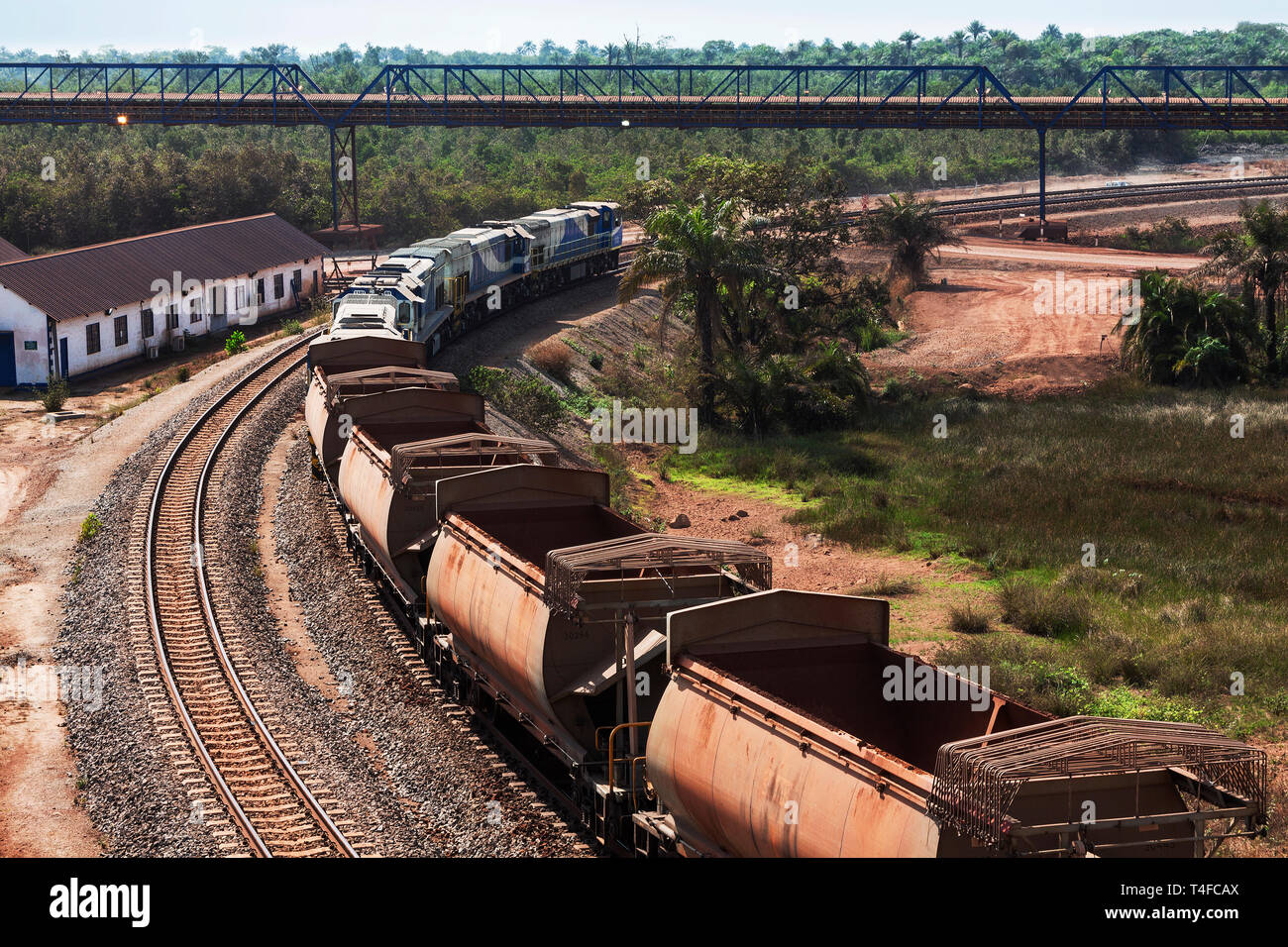 Rail & port operations for managing & transporting iron ore. Train on rail loop under loading jetty conveyor belt after discharge, with empty wagons Stock Photo