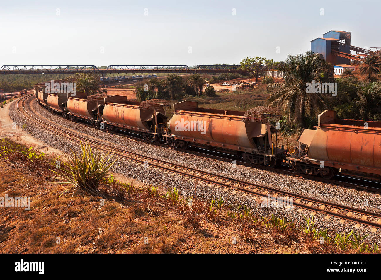 Rail & port operations for managing & transporting iron ore. Train on rail loop under loading jetty conveyor belt after discharge, with empty wagons Stock Photo