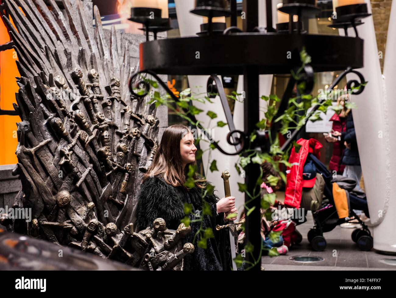 London, England, 16.04.2019.  A Game of Thrones fan poses for a photo sitting on the famous iron throne in Kings Cross station in Central London, following the premiere of the final season of GoT. Credit: Ernesto Rogata/Alamy. Stock Photo