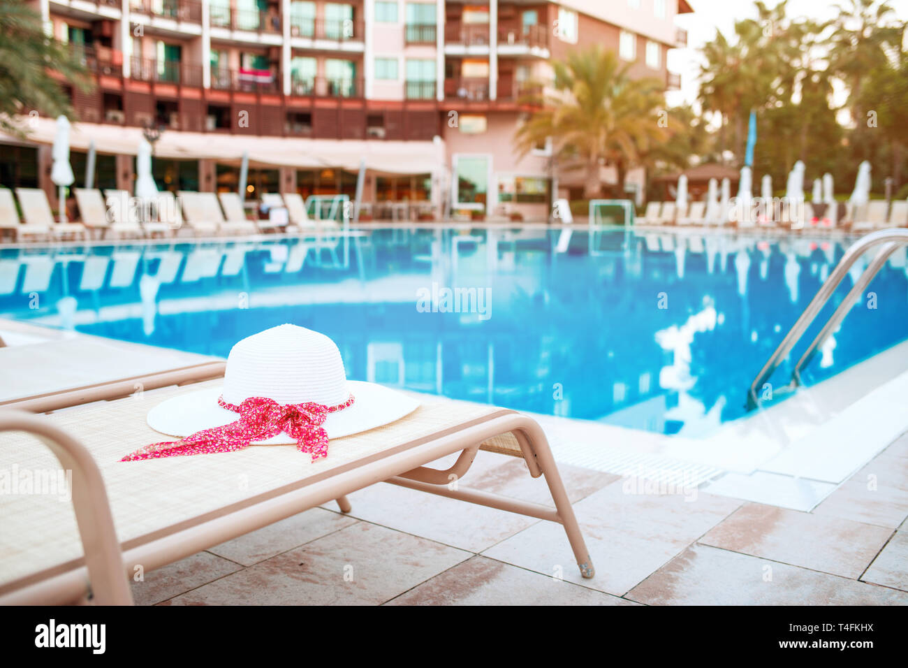 Summer hat lying on deck chair in front of swimming pool. Stock Photo