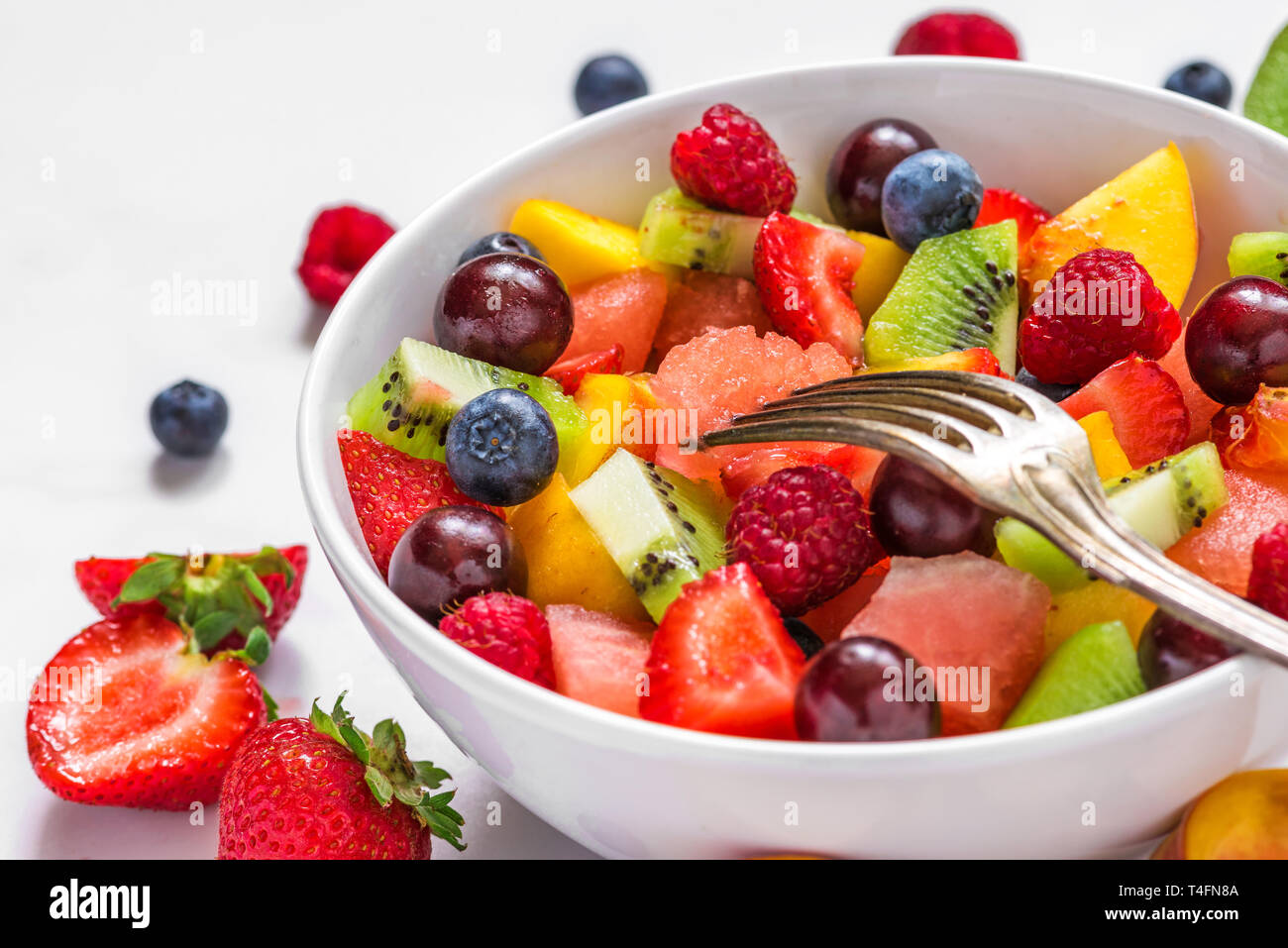 fruit salad with watermelon, strawberry, cherry, blueberry, kiwi, raspberry and peaches in a bowl with fork. healthy vegan food. close up Stock Photo