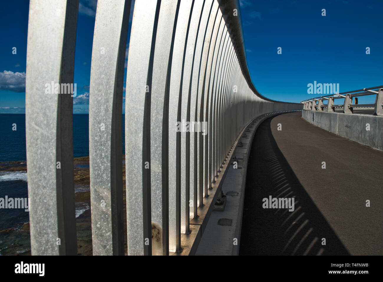 Gaps in the railing reveal some glimpses of Sea Cliff Bridge Ocean Views with Blue Skies. Stock Photo