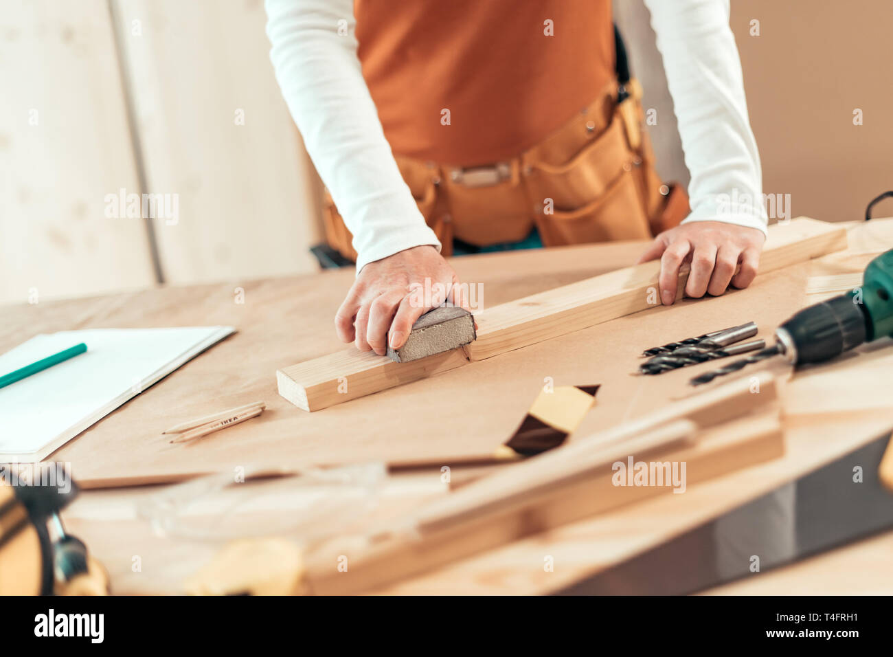 Female carpenter manually sanding wooden plank woth sponge sander in small business woodwork workshop, selective focus Stock Photo