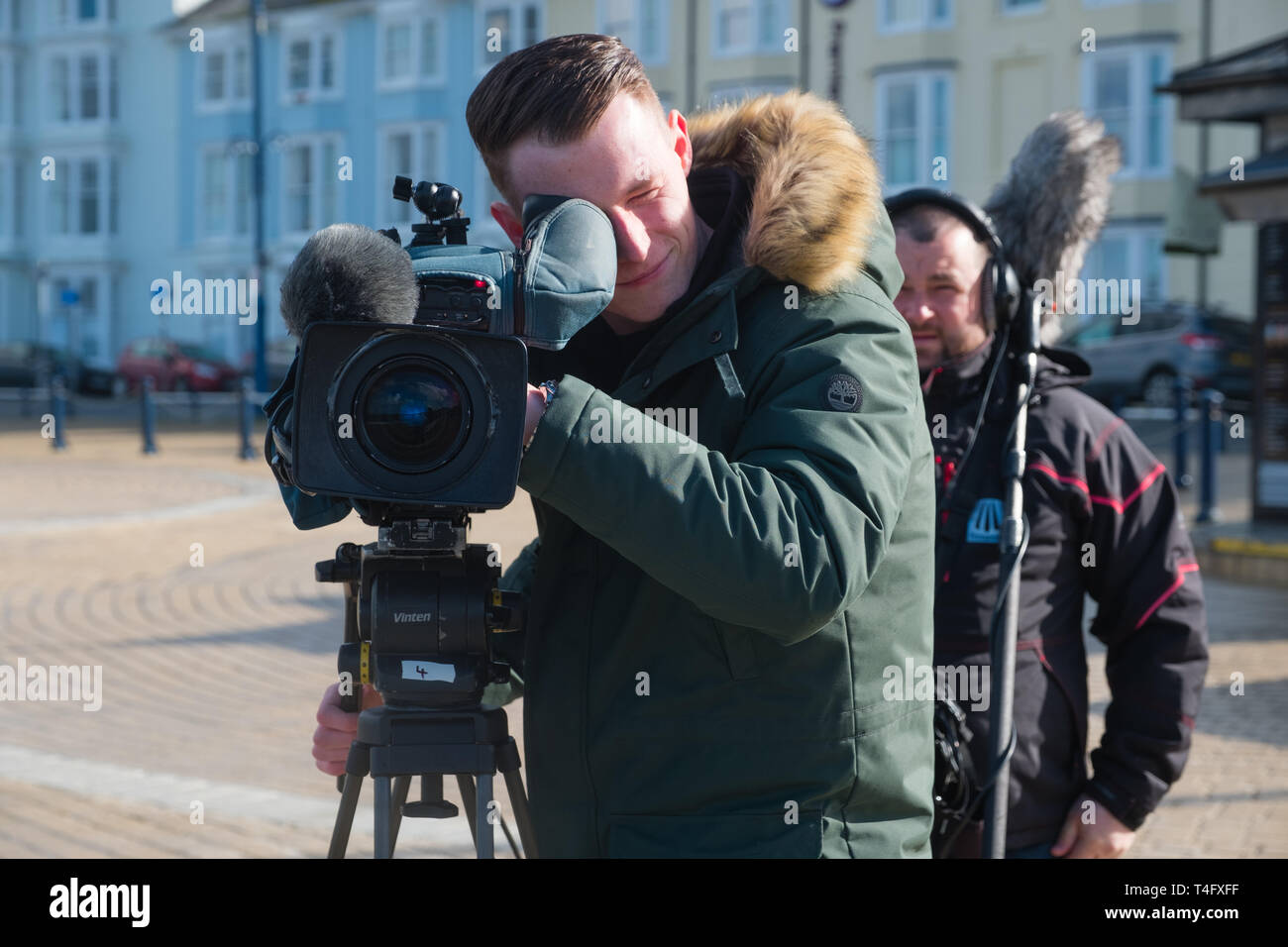 Media workers in the UK: A professional television crew  on location recording an item for broadcast, with the video camerman pointing his lens directly at the subject. UK Stock Photo