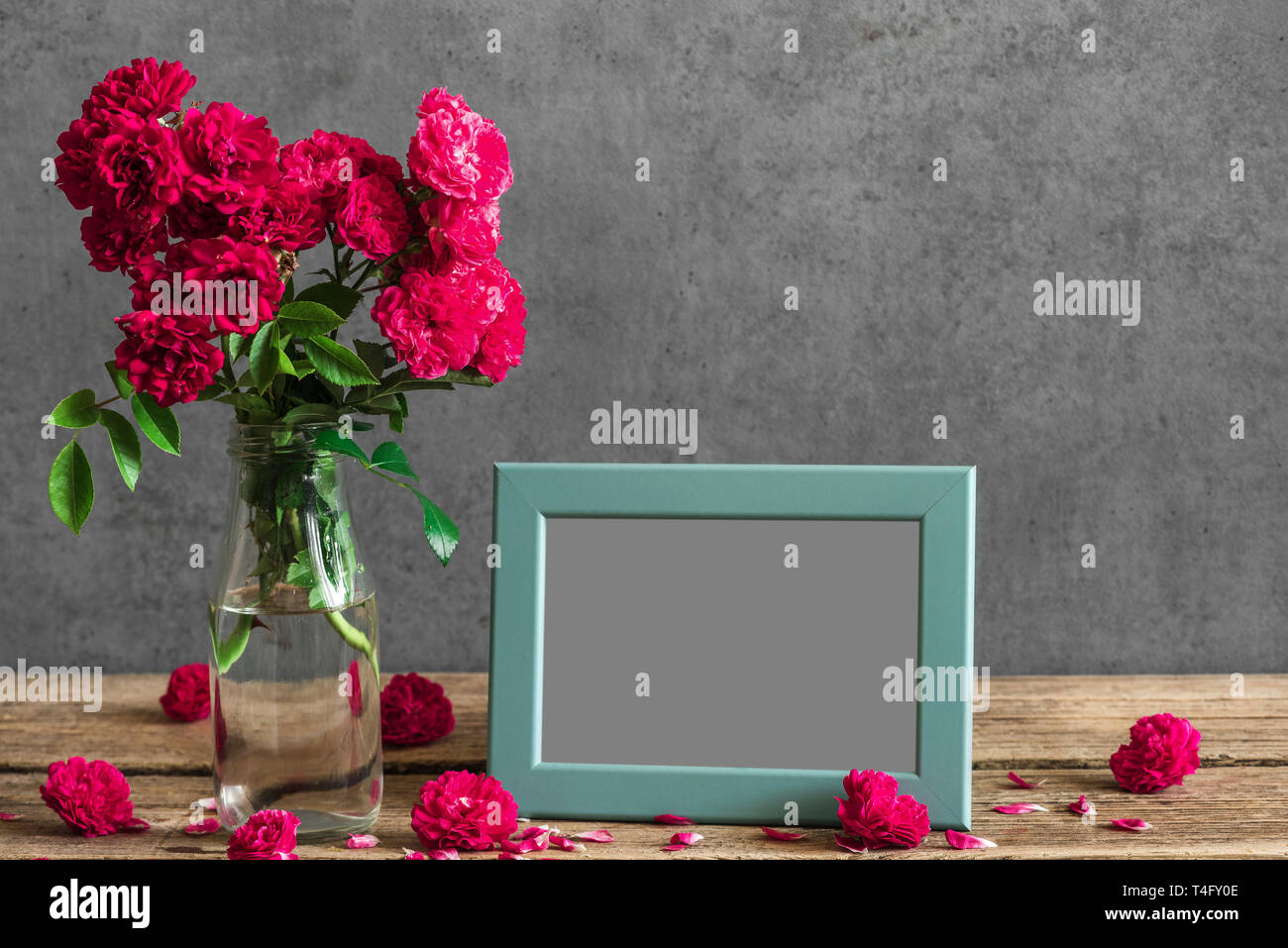 Still life with bouquet of red rose flowers, blank photo frame and buds. mock up. holiday or wedding background Stock Photo