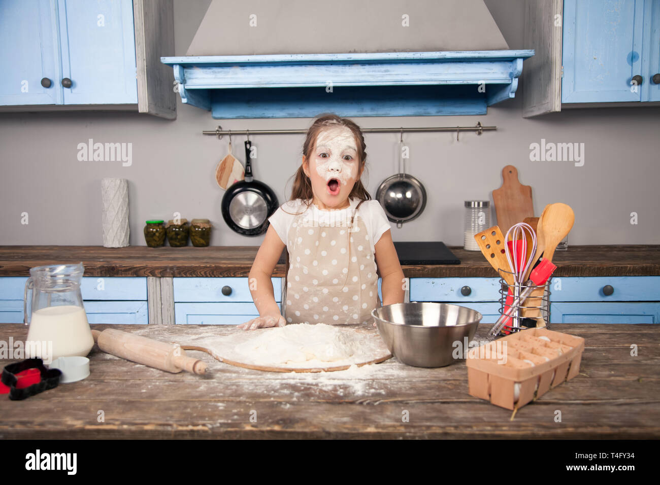 Little child daughter girl is helping her mother in the kitchen to make bakery, cookies. She has a flood all over her face. Fun cooking, homemade food Stock Photo