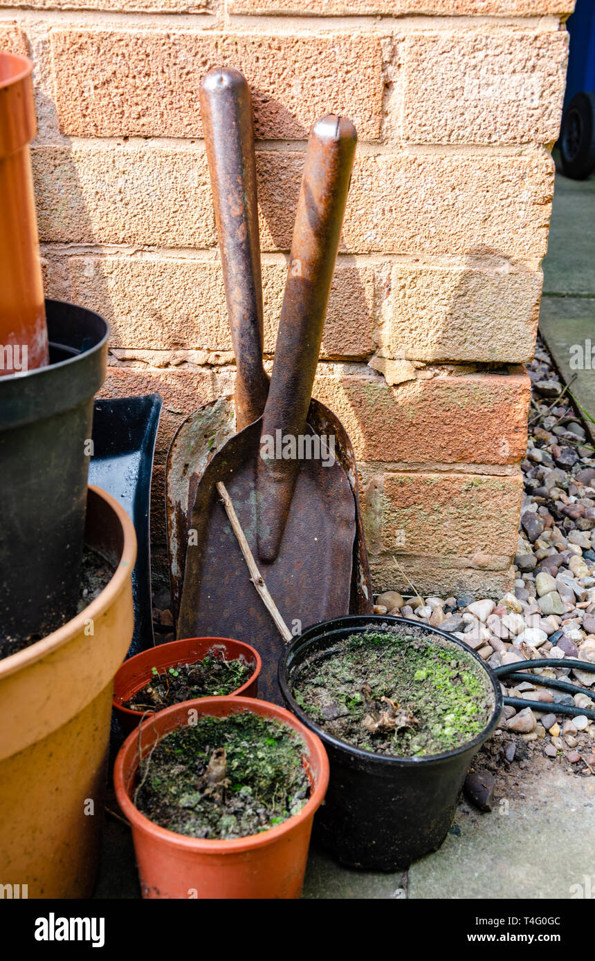 A couple of small hand shovels propped up against a house wall with some plant pots in a residential back garden. Stock Photo