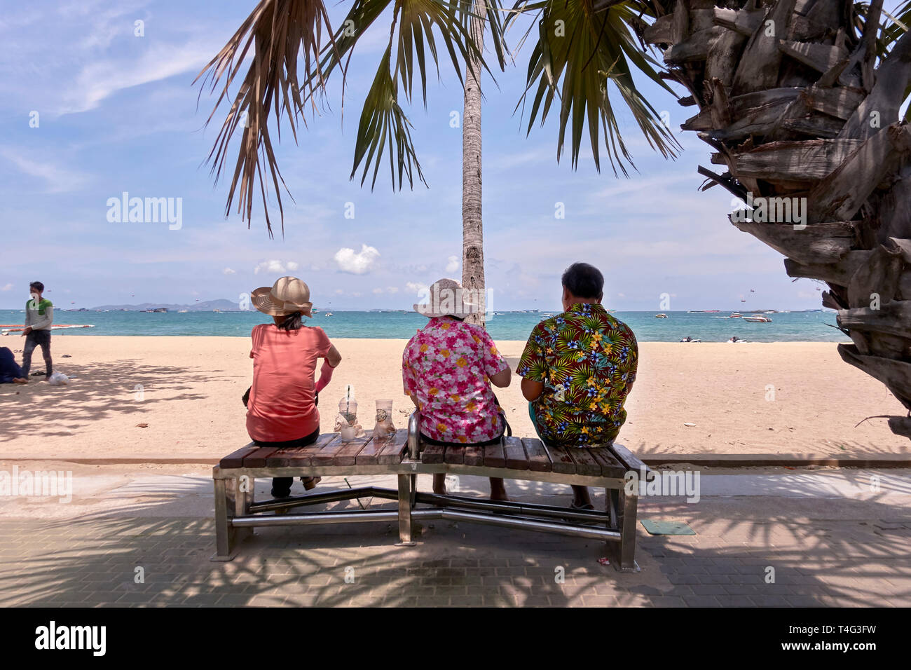 Three people. Man and two female companions sitting on a bench and overlooking the ocean at Pattaya beach, Thailand, Southeast Asia Stock Photo