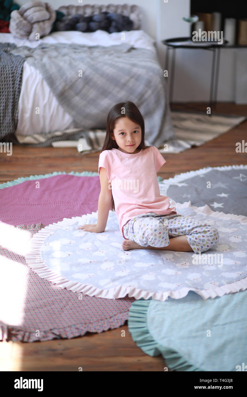 Child girl sits on the floor on the round mat against the bed