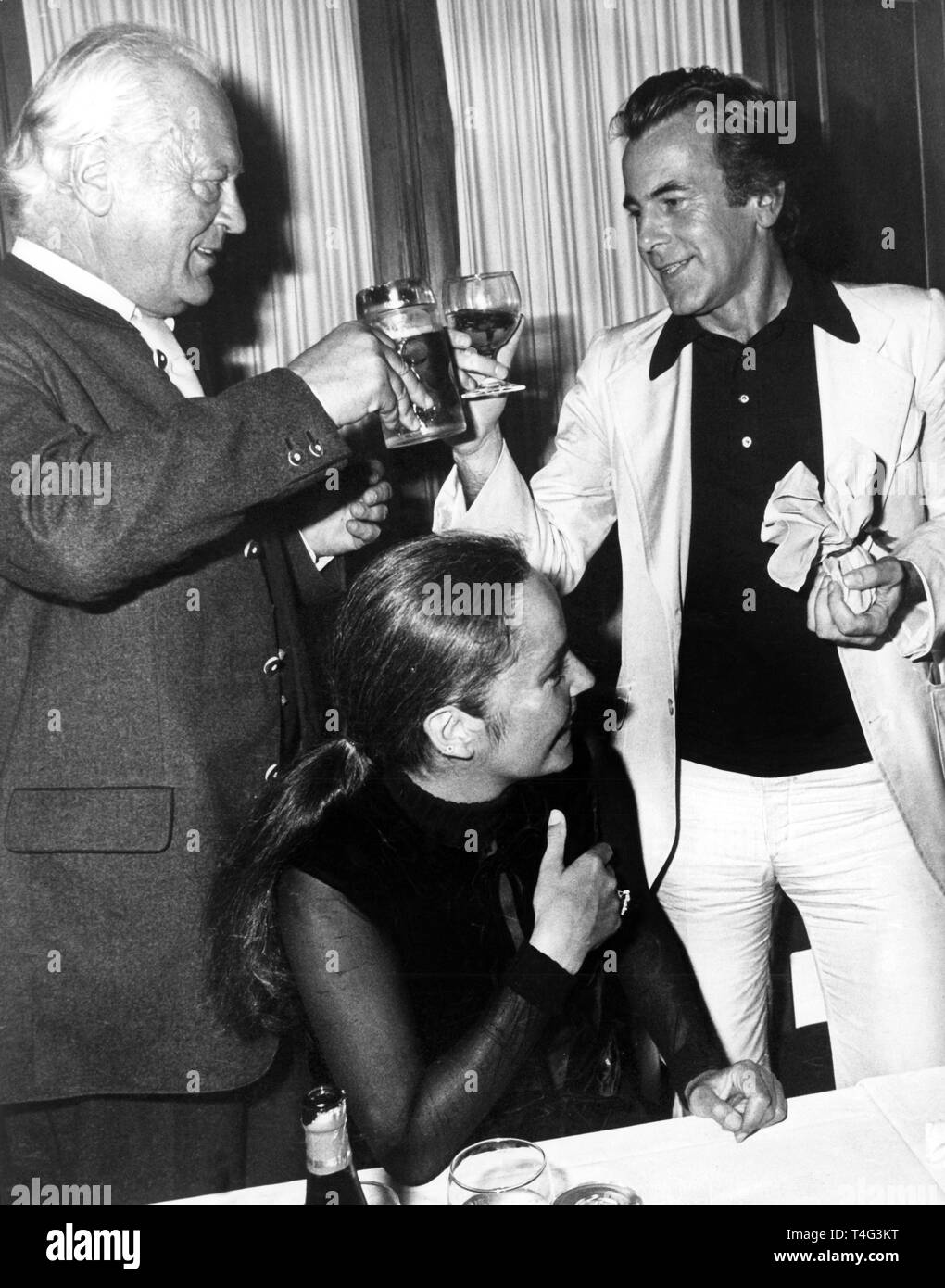Curd Jürgens (l) and Maximilian Schell (r) raise their glasses to each other, in the centre Margie Jürgens, at the final party after the 'Jedermann' performance during the Salzburg Festival at castle Klessheim on 28 August 1977. | usage worldwide Stock Photo