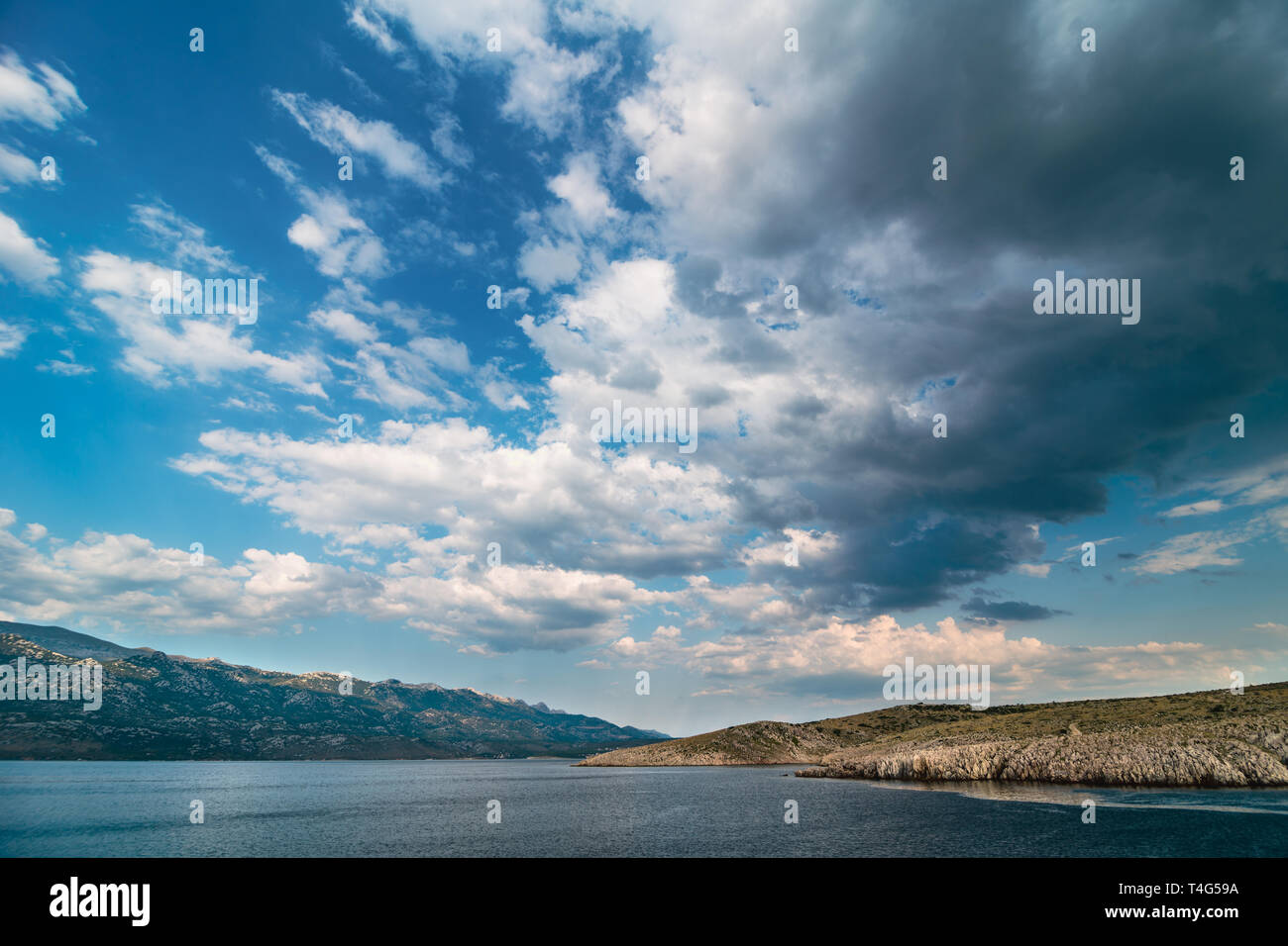 Beautiful ocean and dramatic blue sky with clouds on hot summer day., rain in background over Paklenica National Park Mountains. Stock Photo