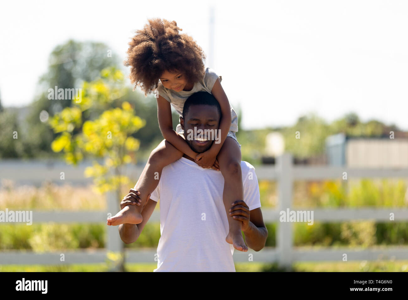 Smiling African American man carrying daughter on shoulders Stock Photo