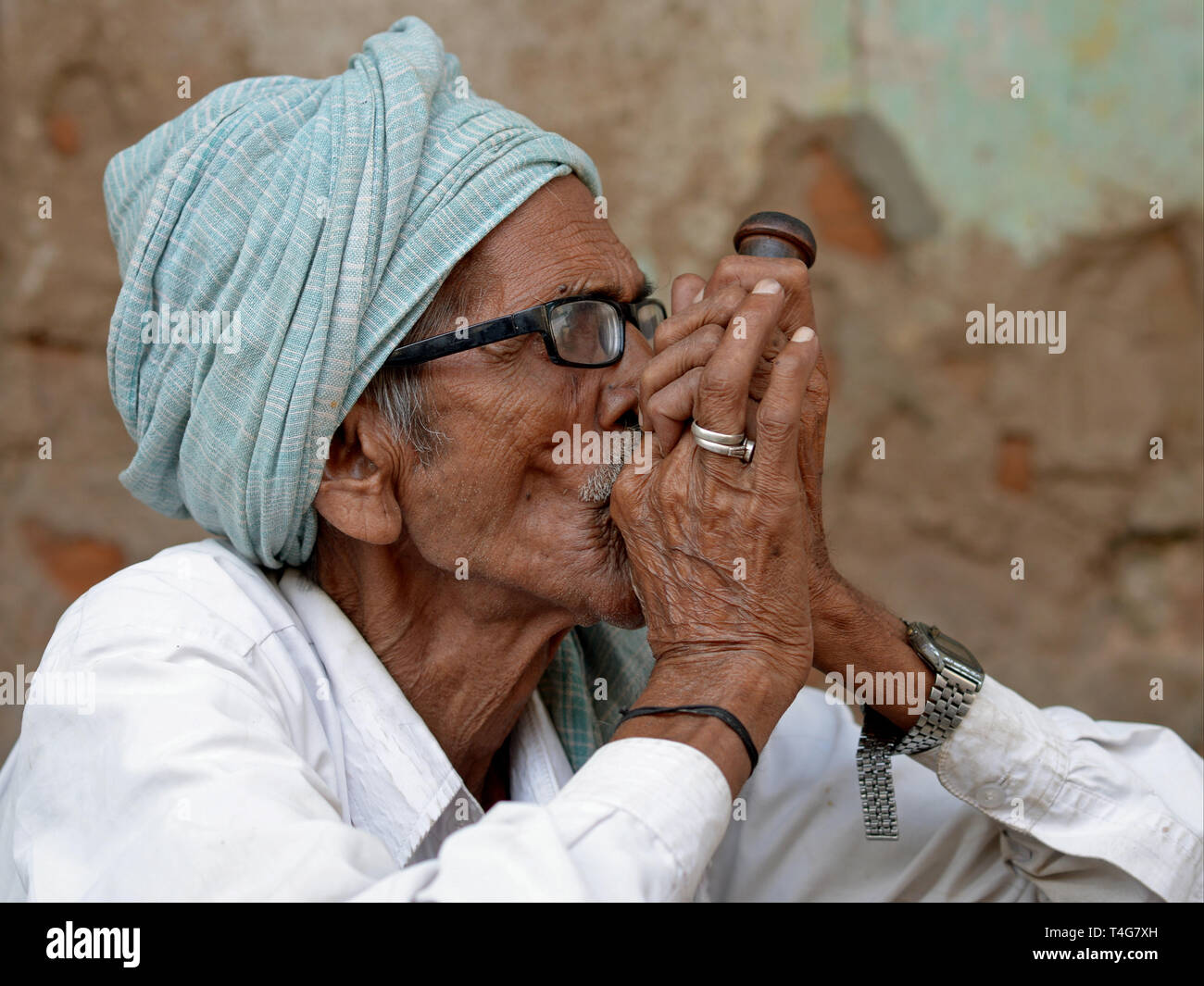 Old Indian Rajasthani man smokes tobacco in his chillum pipe. Stock Photo