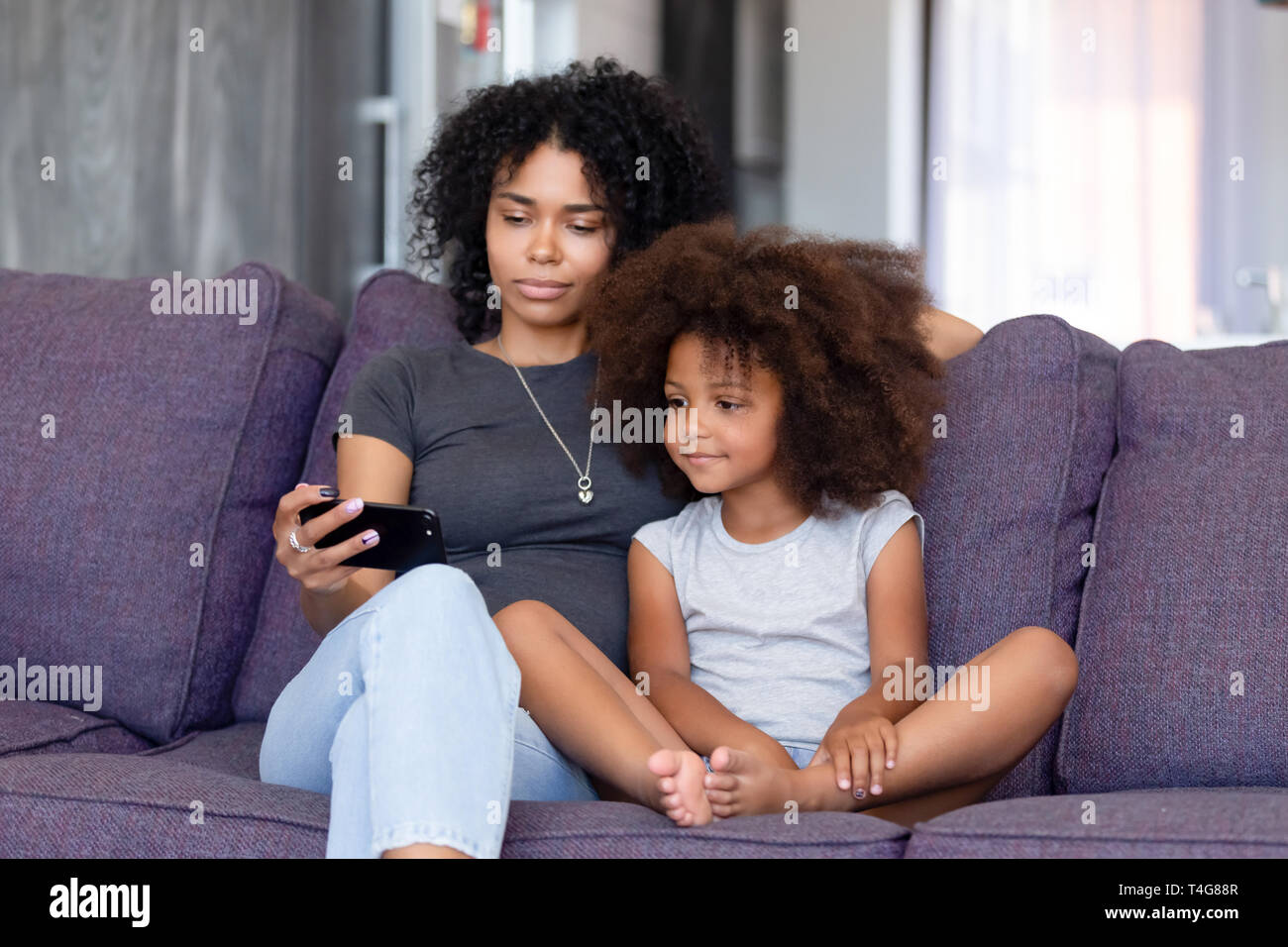 African American woman with daughter using phone together at home Stock Photo