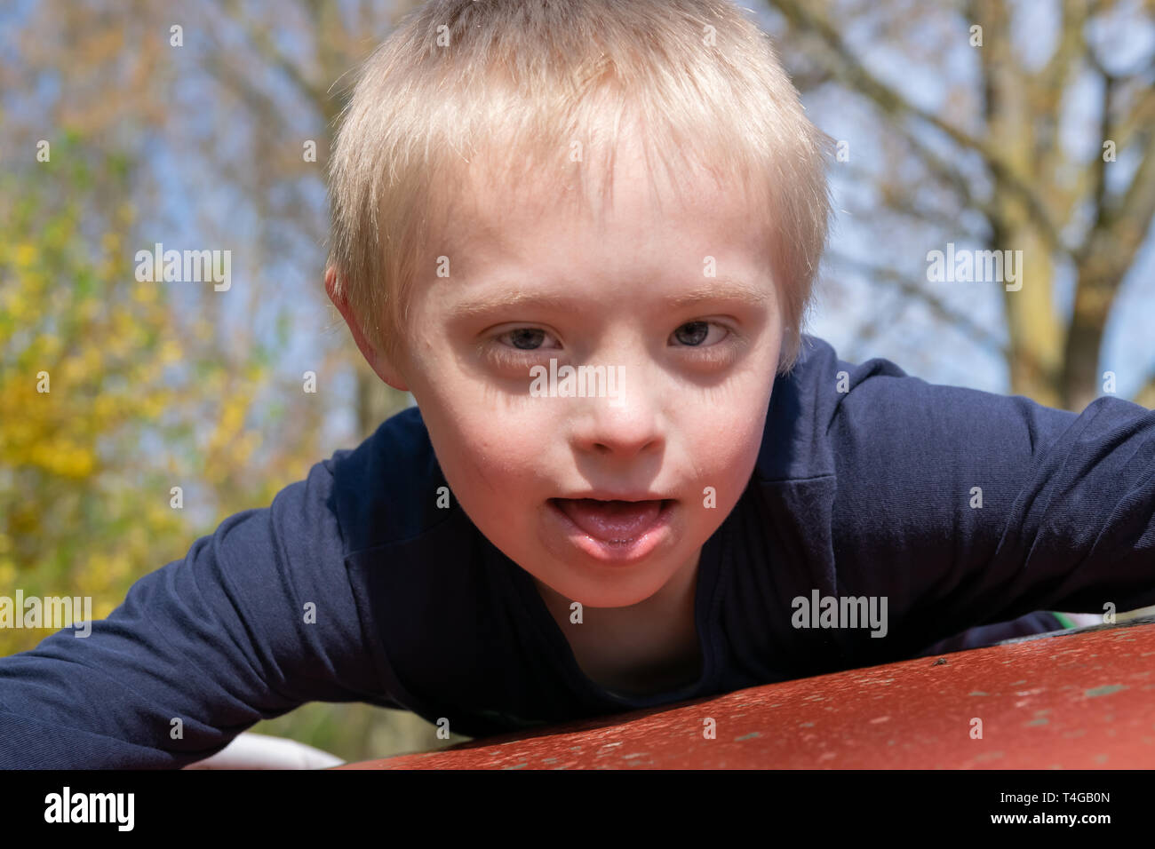 Defect,childcare,medicine and people concept: Blond boy with down syndrome playing in a park at spring time. Stock Photo
