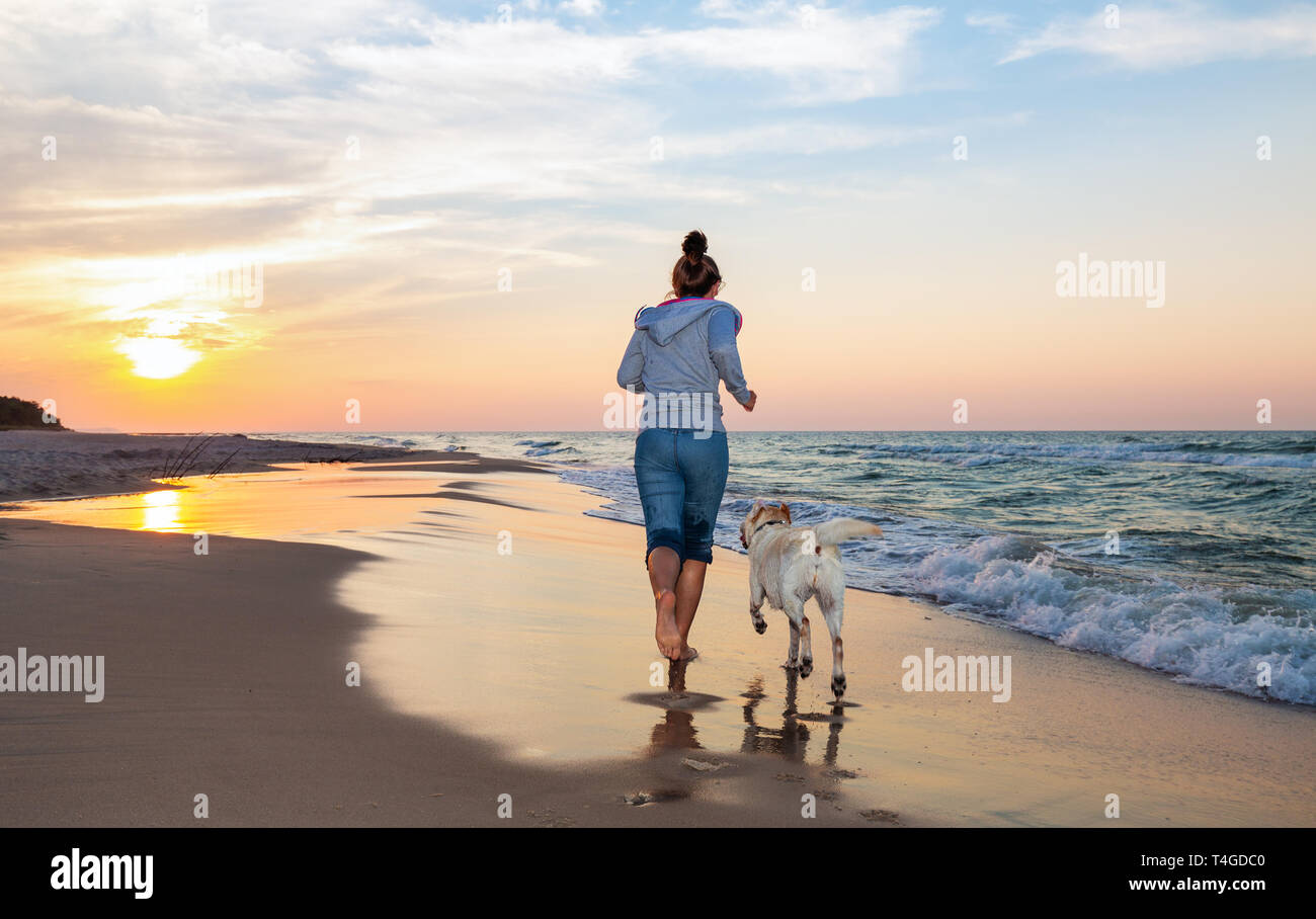 A woman running on the beach with a dog Stock Photo