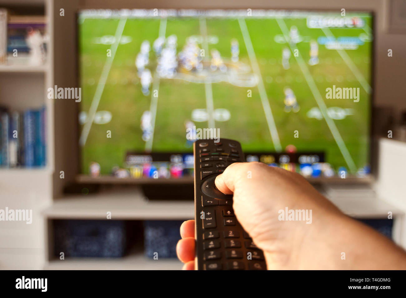 hand holding remote control in front of tv on a sport channel Stock Photo