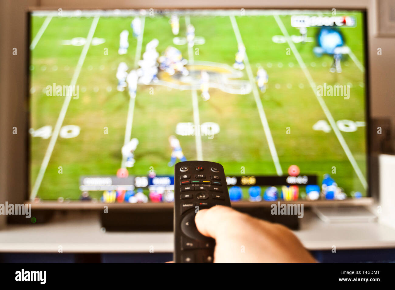 hand holding remote control in front of tv on a sport channel Stock Photo