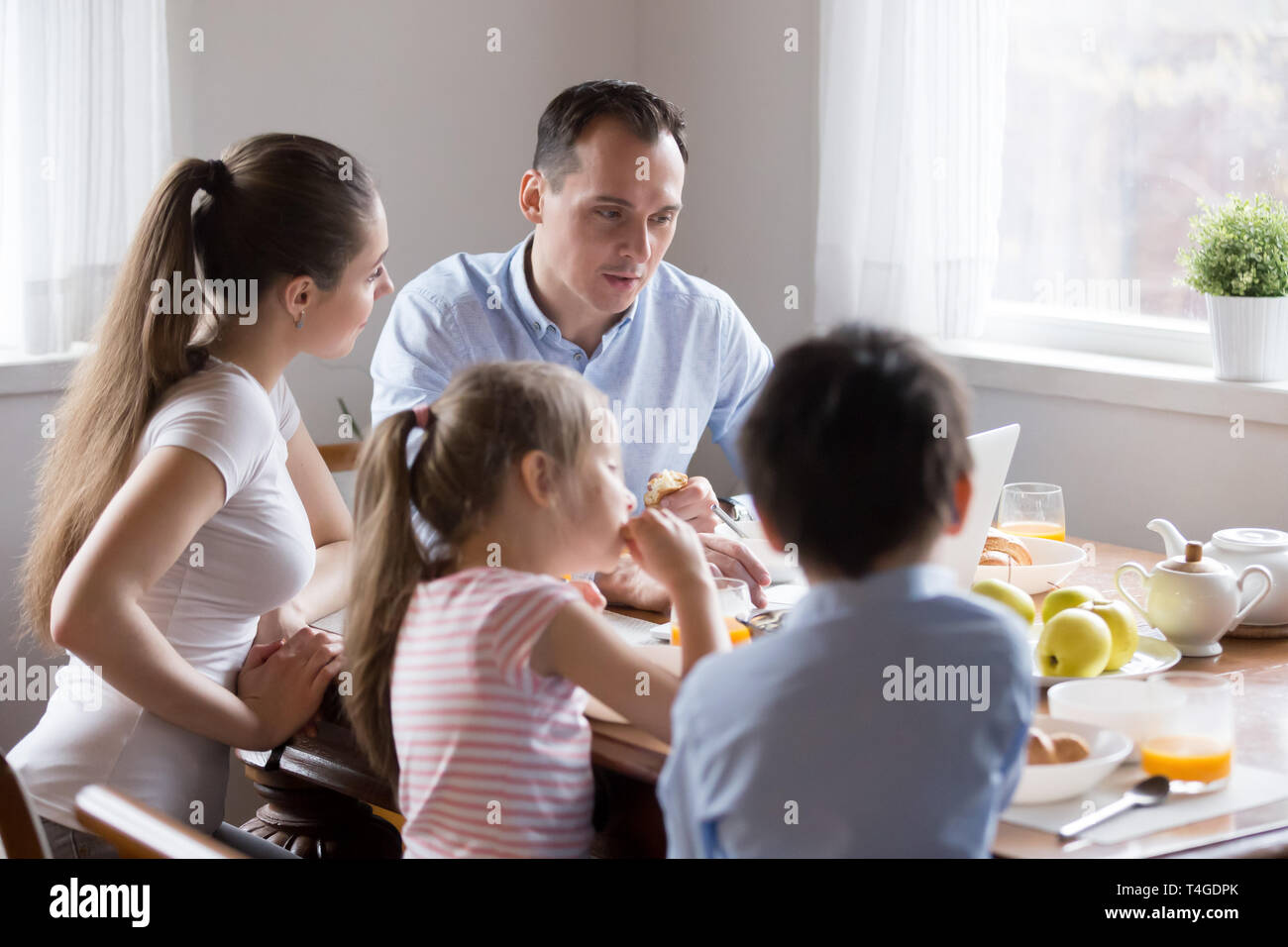 Parents watching computer while children eating breakfast at kitchen Stock Photo