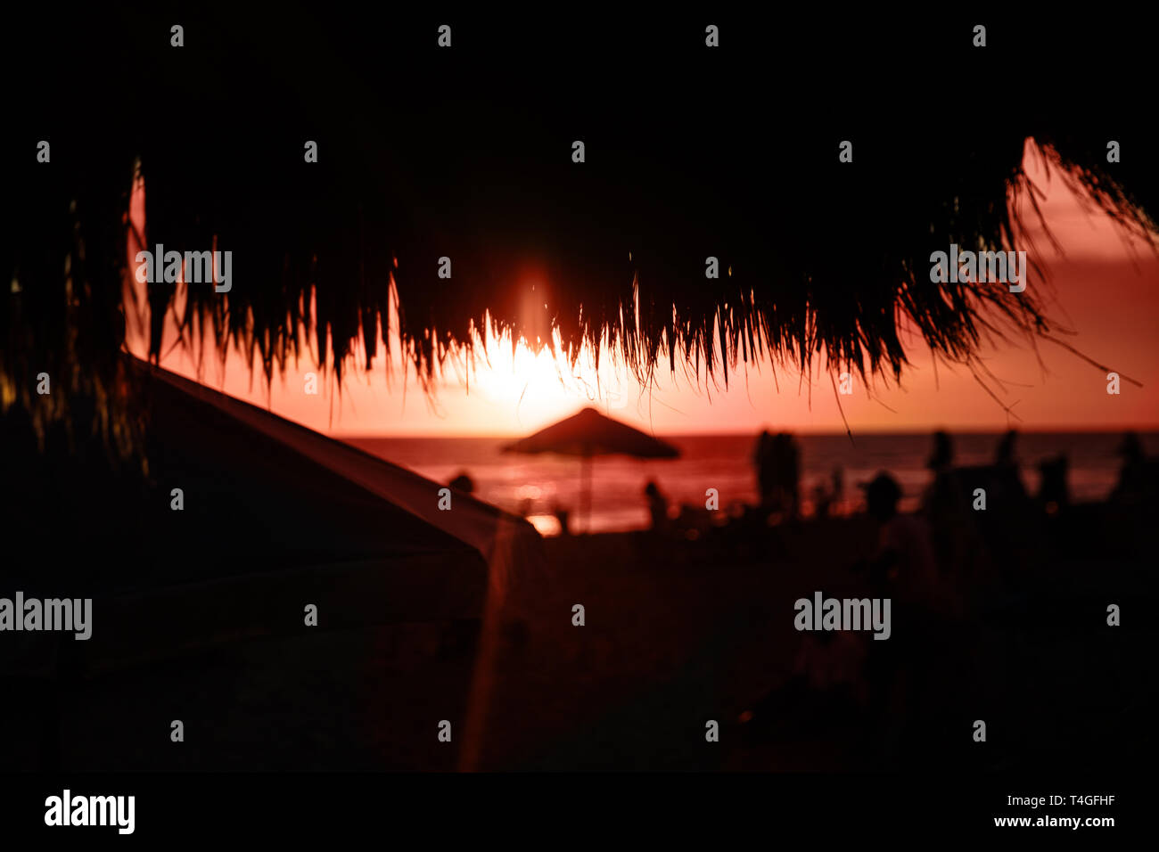 Straw beach roof in the cafe with blurred people on coral sunset. Summer concept. Stock Photo