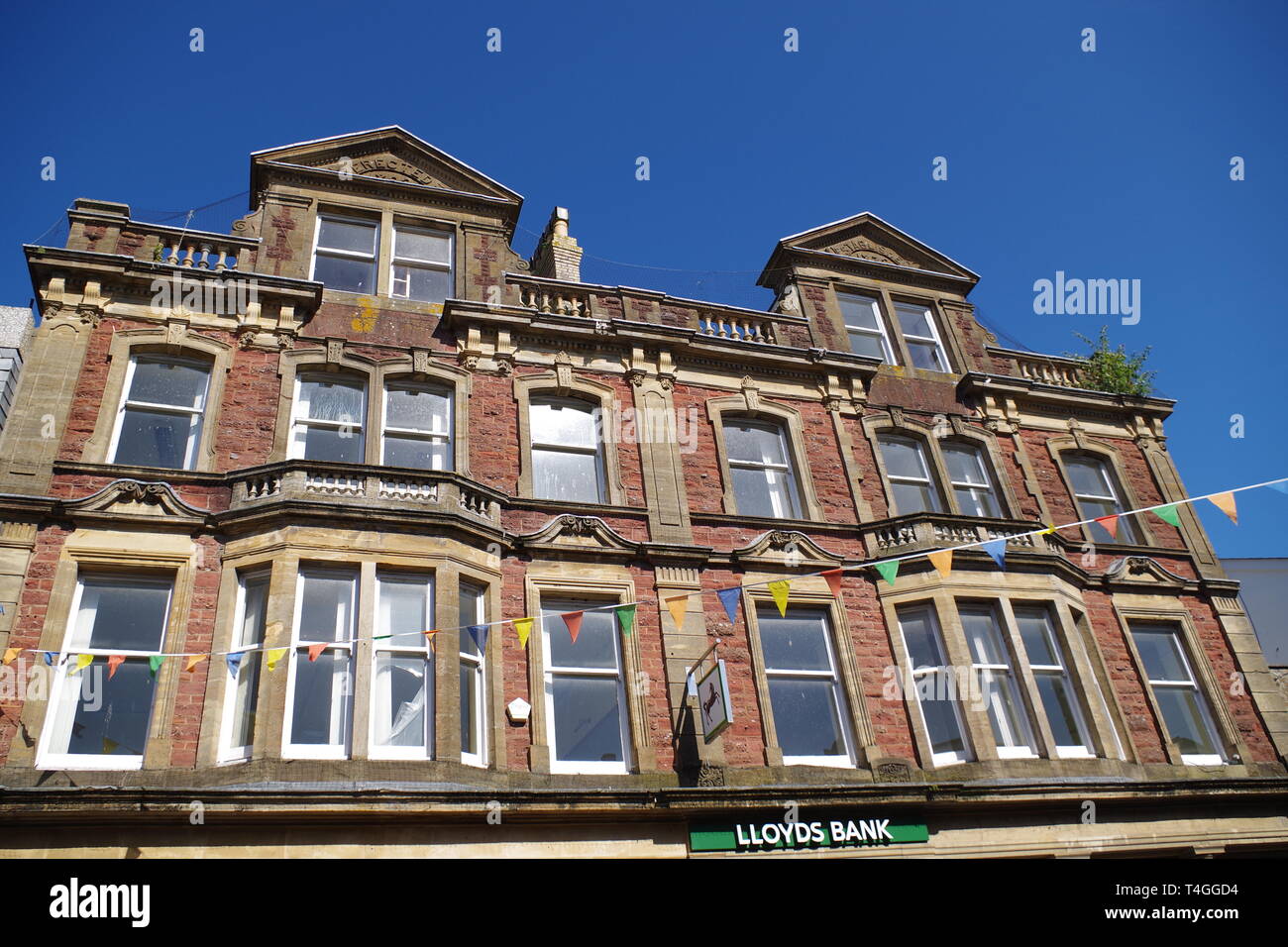 Lloyds Bank, 65 Fore Street, Kingsbridge, Devon, UK. Elegant Victorian Stone Building with Festive Bunting on a Summers Day. Stock Photo