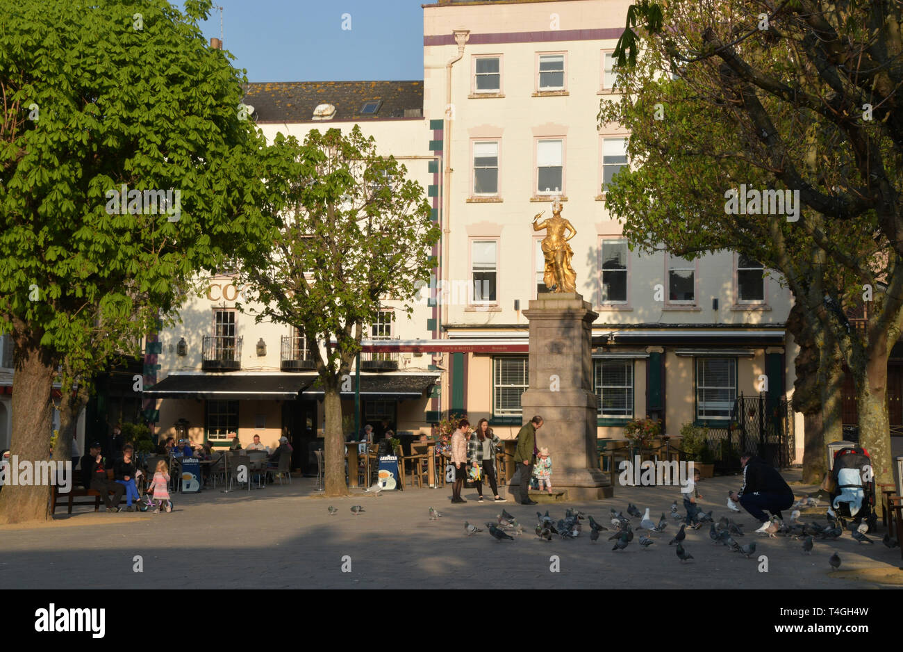 Spring sunshine enjoyed by visitors beneath the statue of King George II in the Royal Square, St Helier,Jersey, Channel islands Stock Photo