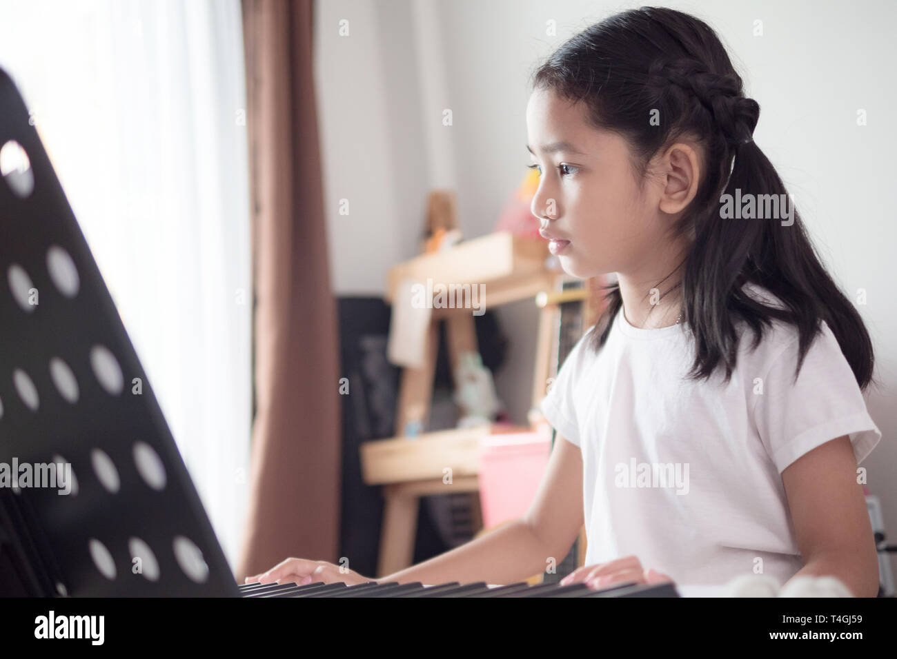 Asian little girl learning to play piano keyboard synthesizer with happiness, Thai girl studying