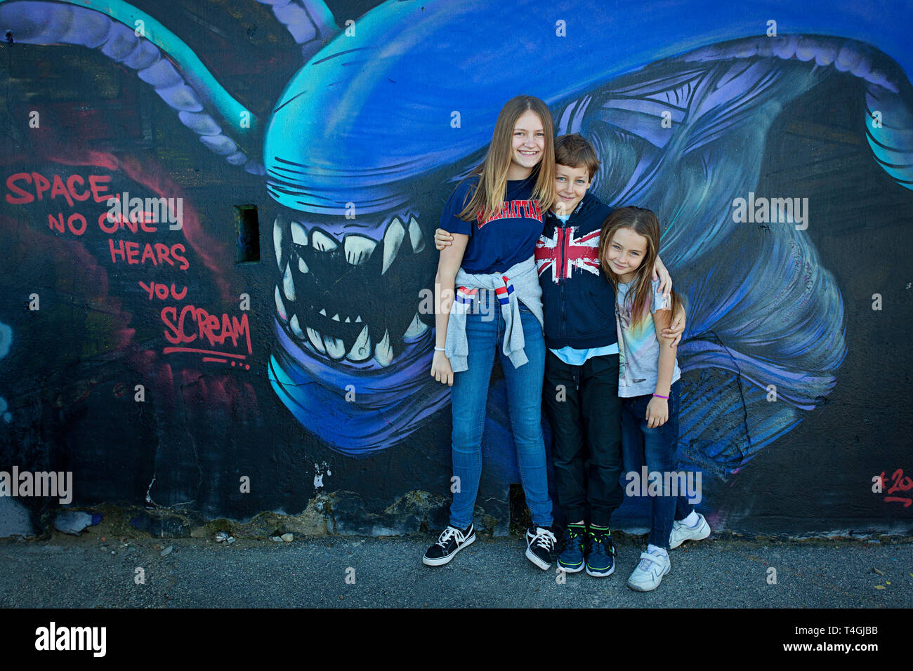 Three kids pose in front of a graffiti wall Stock Photo