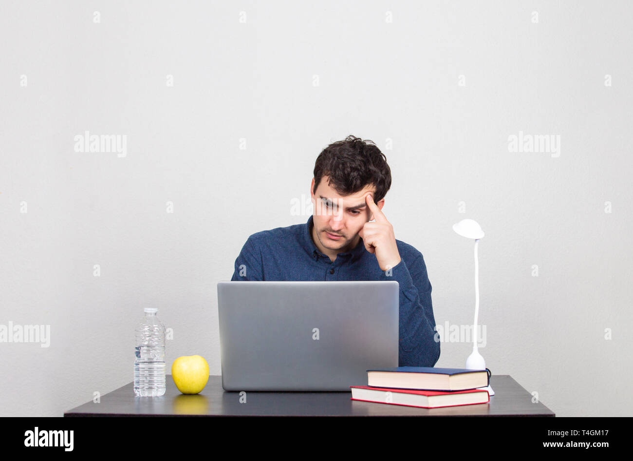 Frustrated and stressed male student thinking intensively looking at a laptop . Tired office worker sitting at desk using computer and doing overtime  Stock Photo