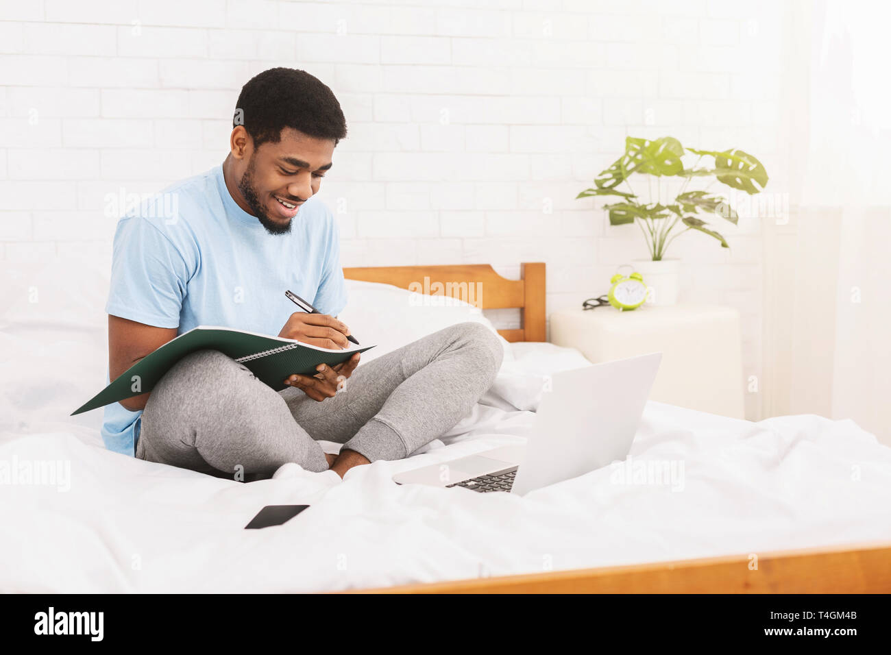 Cheerful black student learning online in bed Stock Photo