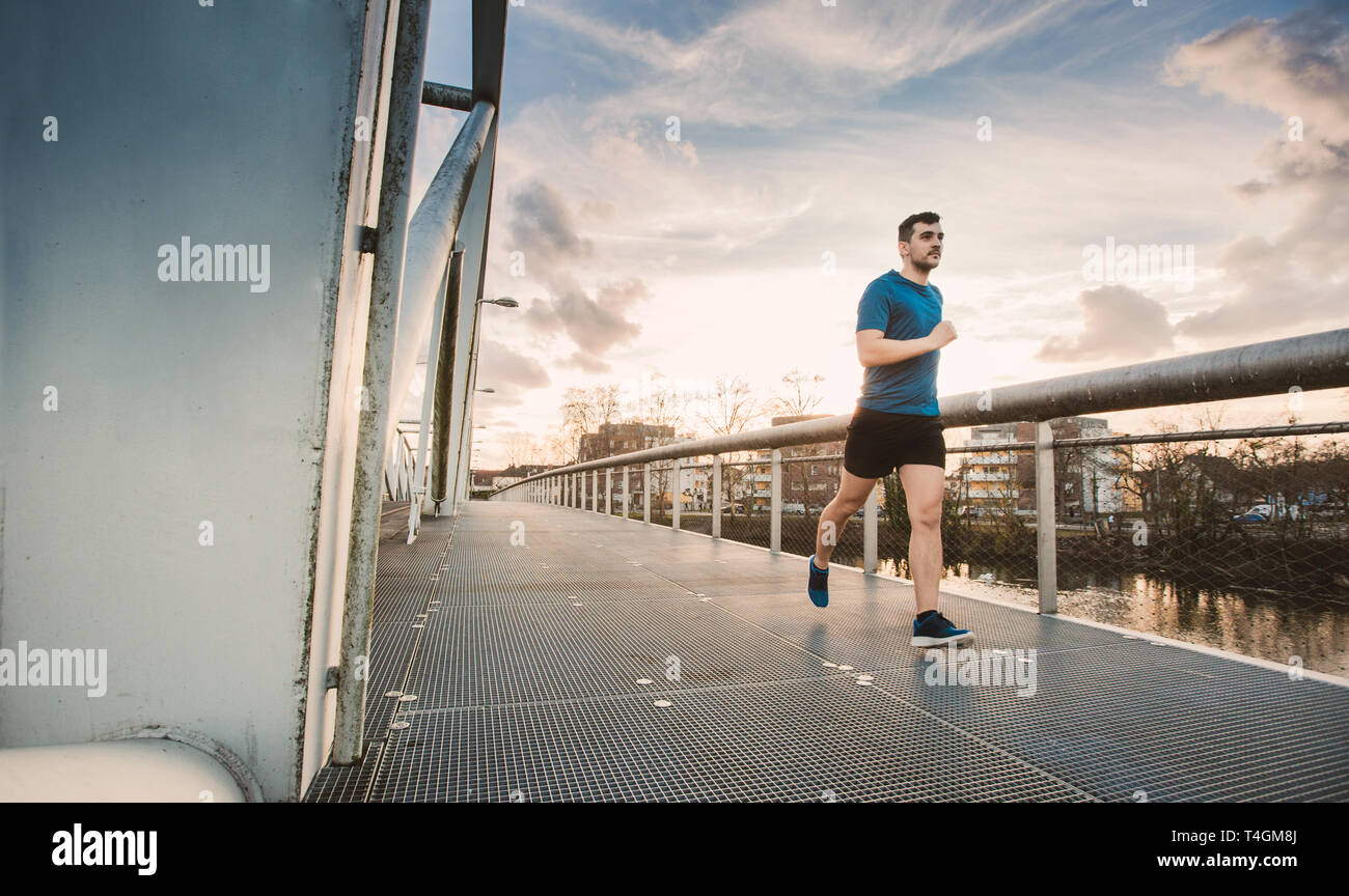 Running man runner training doing outdoor city run sprinting over a bridge. Urban healthy active lifestyle. Male athlete running over sunset backgroun Stock Photo