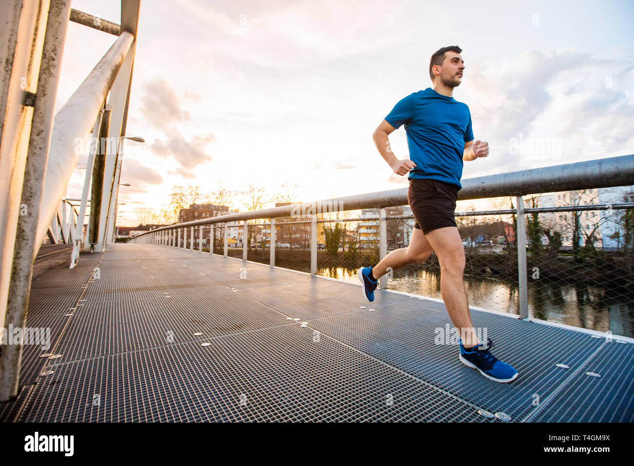Running man runner training doing outdoor city run sprinting over a bridge. Urban healthy active lifestyle. Male athlete running over sunset backgroun Stock Photo