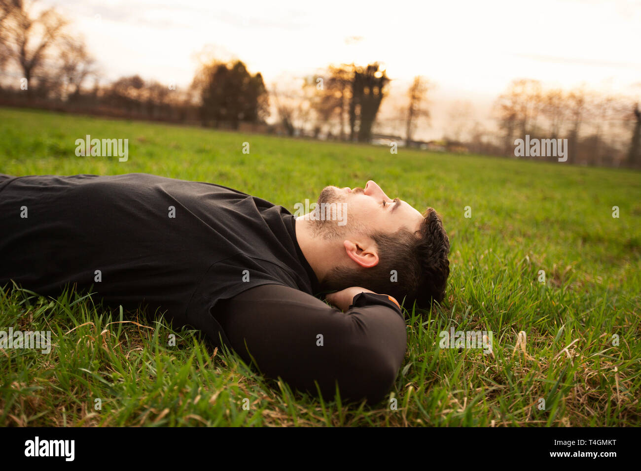 Sport fitness man relaxing  after training outdoor in a city park . Young male athlete resting relaxing lying on grass after long run and training exe Stock Photo
