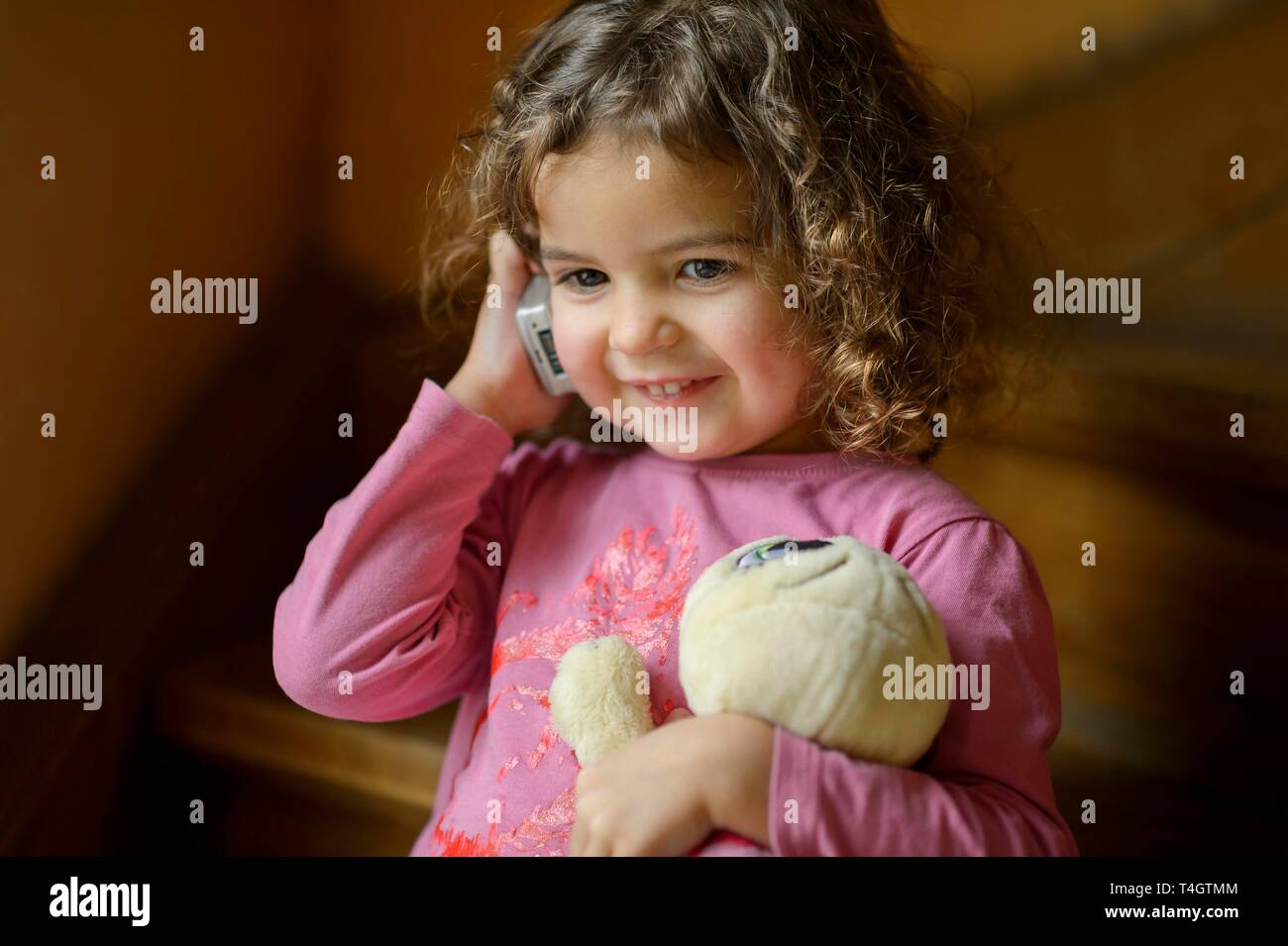 Girl, 3 years, portrait, sits smiling on the stairs with mobile phone, phoned, Germany Stock Photo