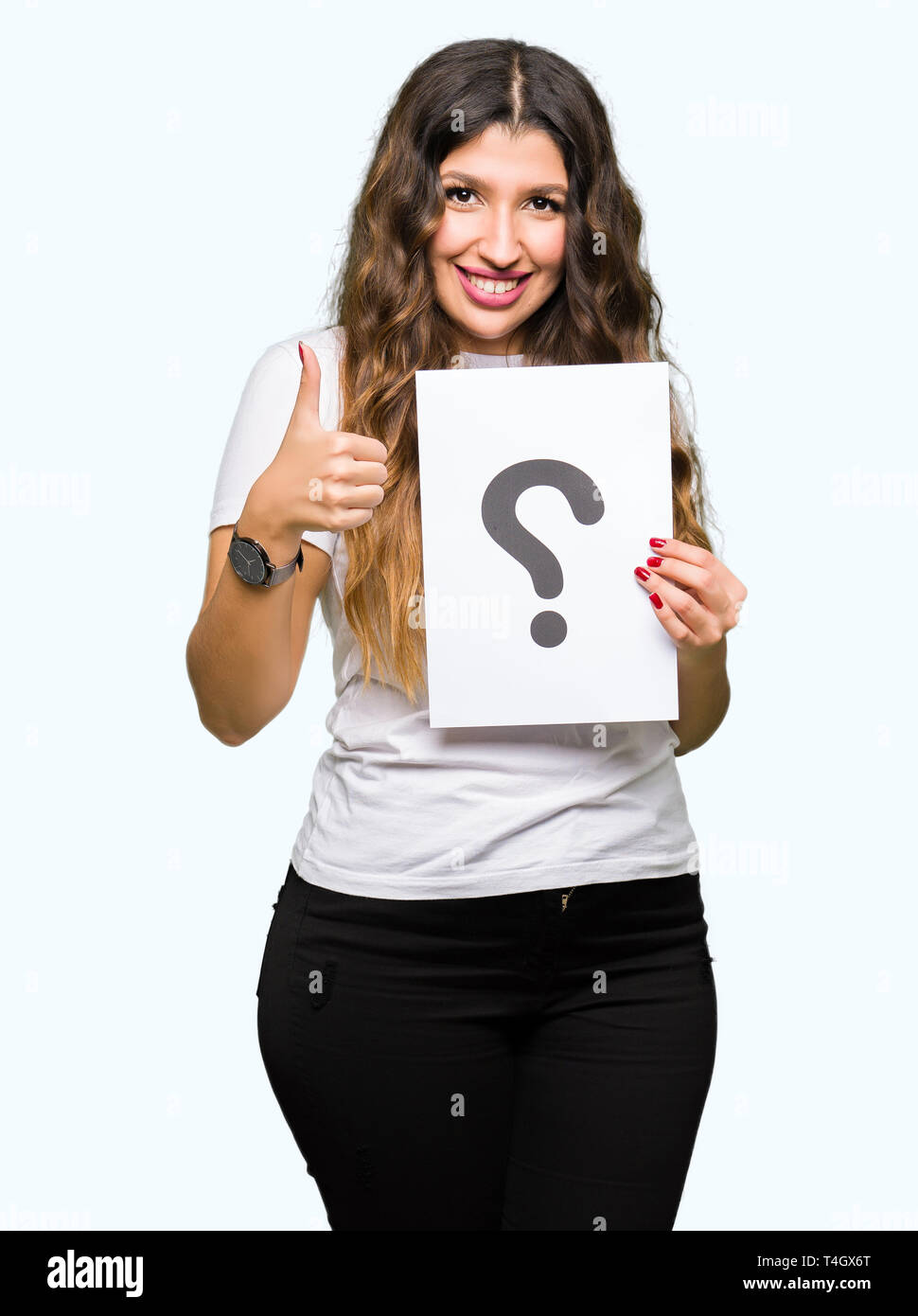 Young adult woman holding paper with question mark happy with big smile doing ok sign, thumb up with fingers, excellent sign Stock Photo
