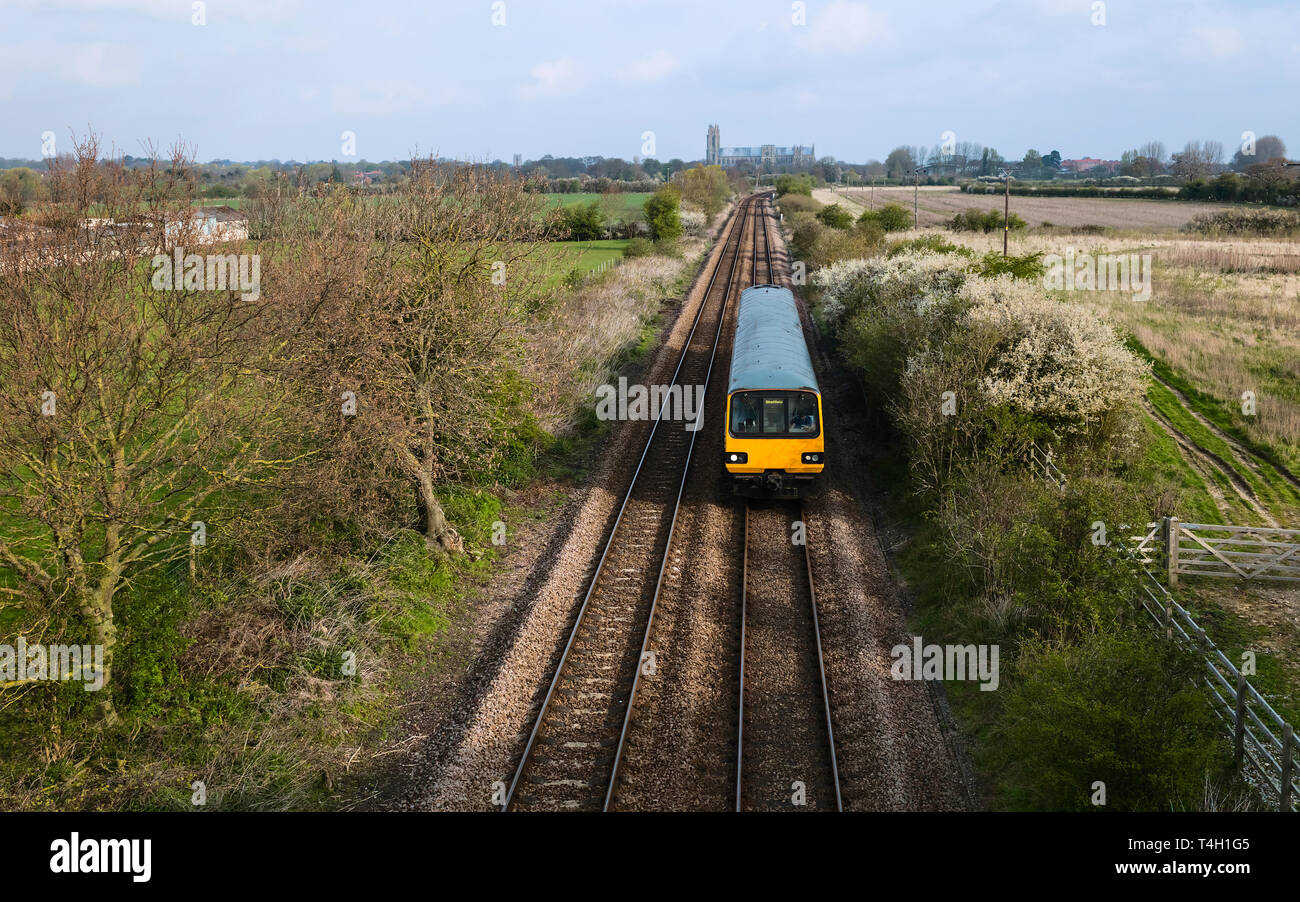 A railway train cuts through rural landscape on a bright autumn day with ancient minster on horizon near Beverley, Yorkshire, Stock Photo