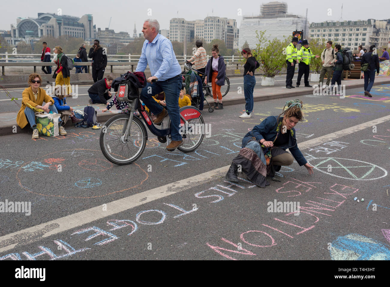 A commuter cycles past Climate Change activists with Extinction Rebellion campaigning for a better future for planet Earth after blocking Waterloo Bridge and as part of a multi-location 5-day Easter protest around the capital, on 16th April 2019, in London, England. Stock Photo