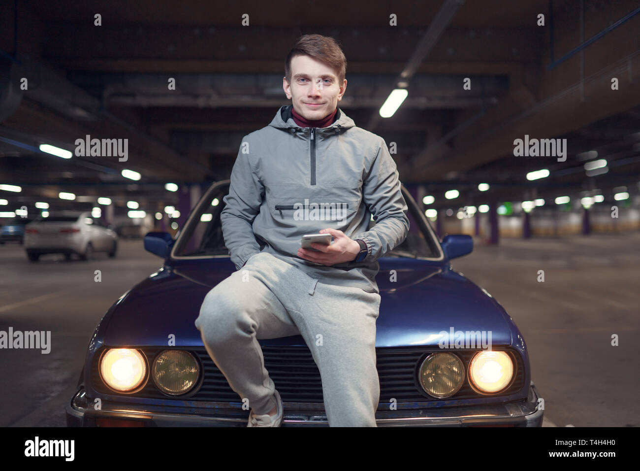 Image of man with phone sitting on hood of black car Stock Photo Alamy