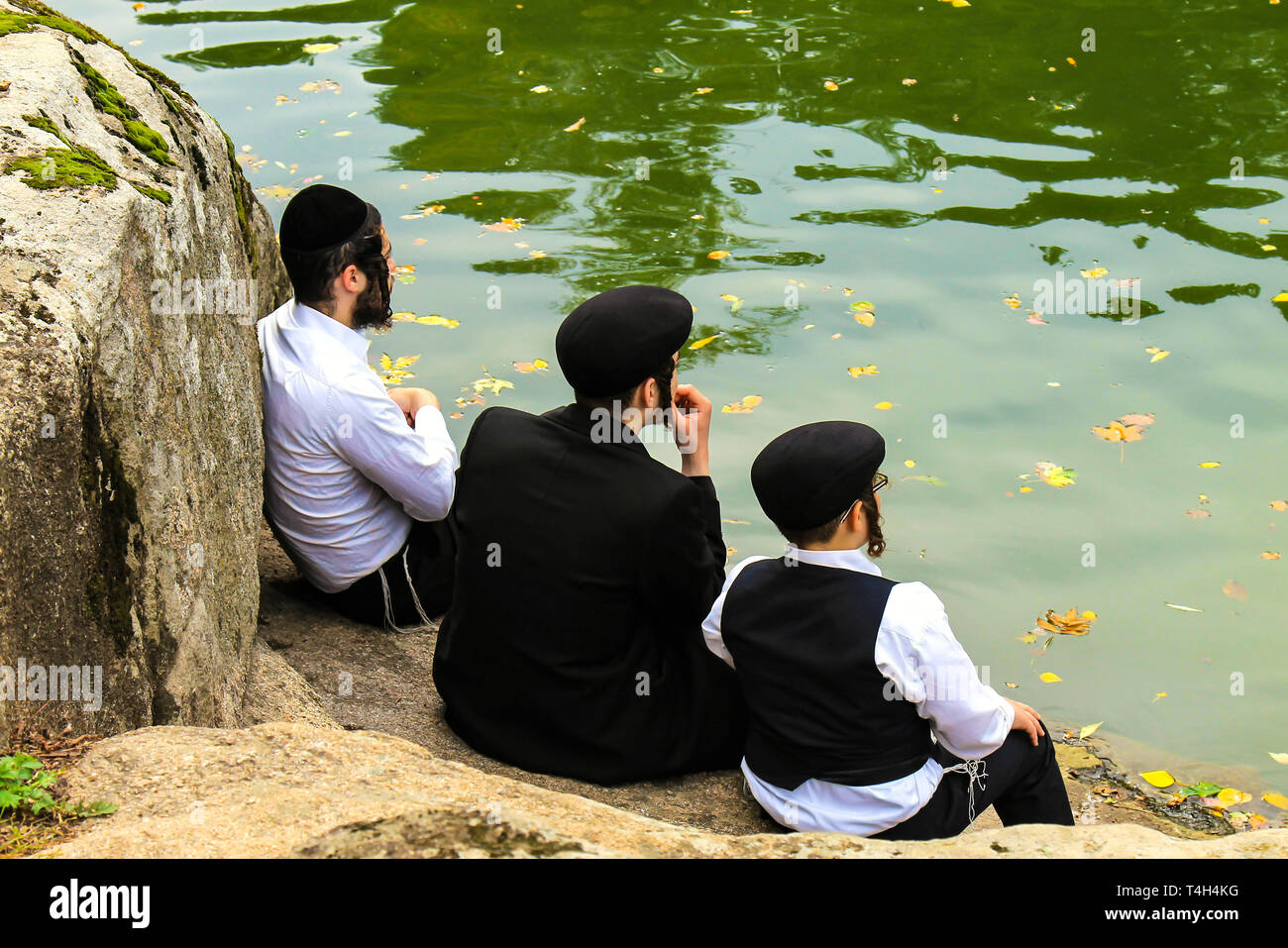 A family of Hasidic Jews, 3 boys, black clothes sitting in the autumn park, the time of the Jewish New Year. Stock Photo