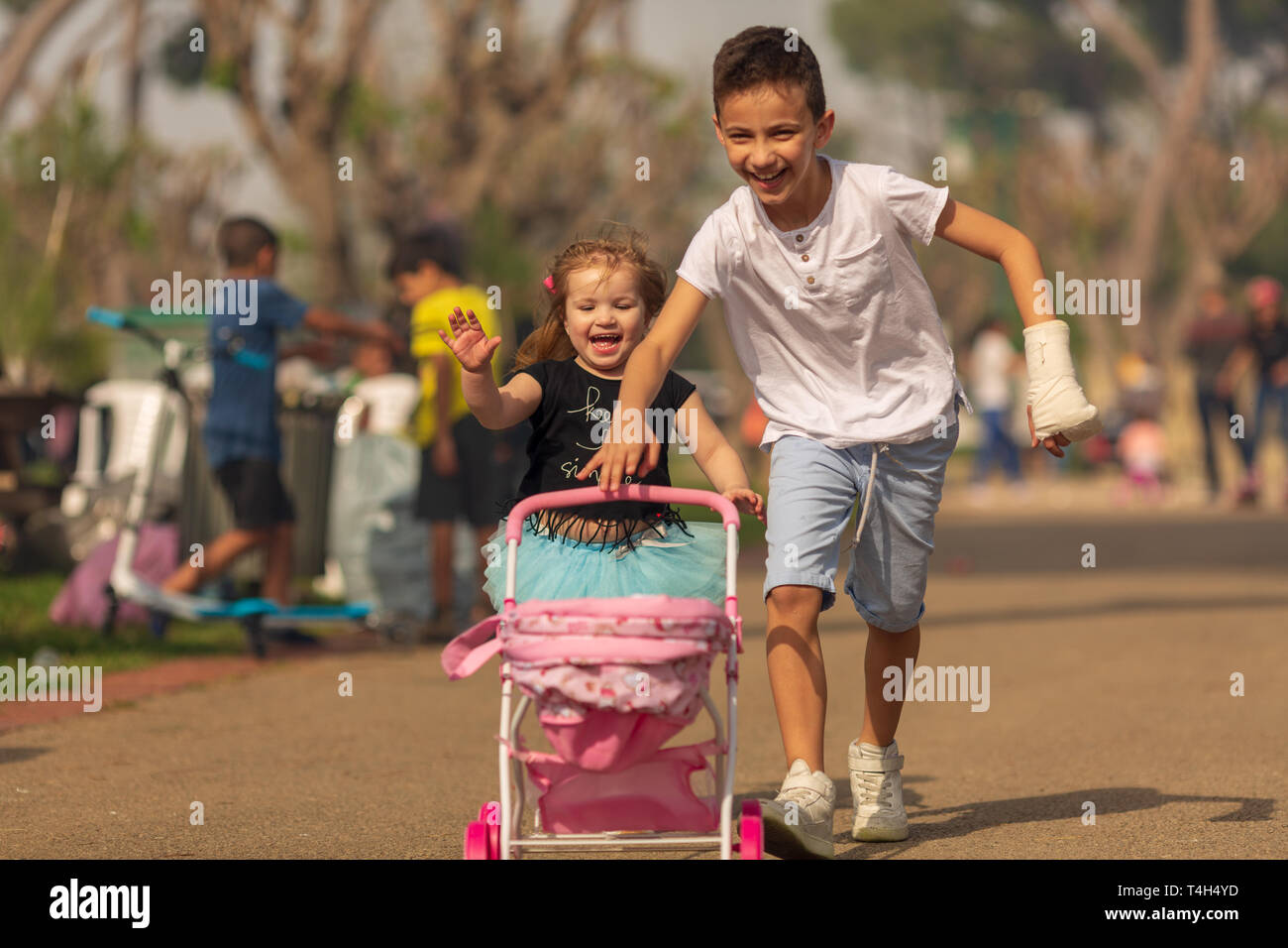 boy and girl play a game of children playing in a pram in a park. Children's friendship. Children with a toy pram Stock Photo