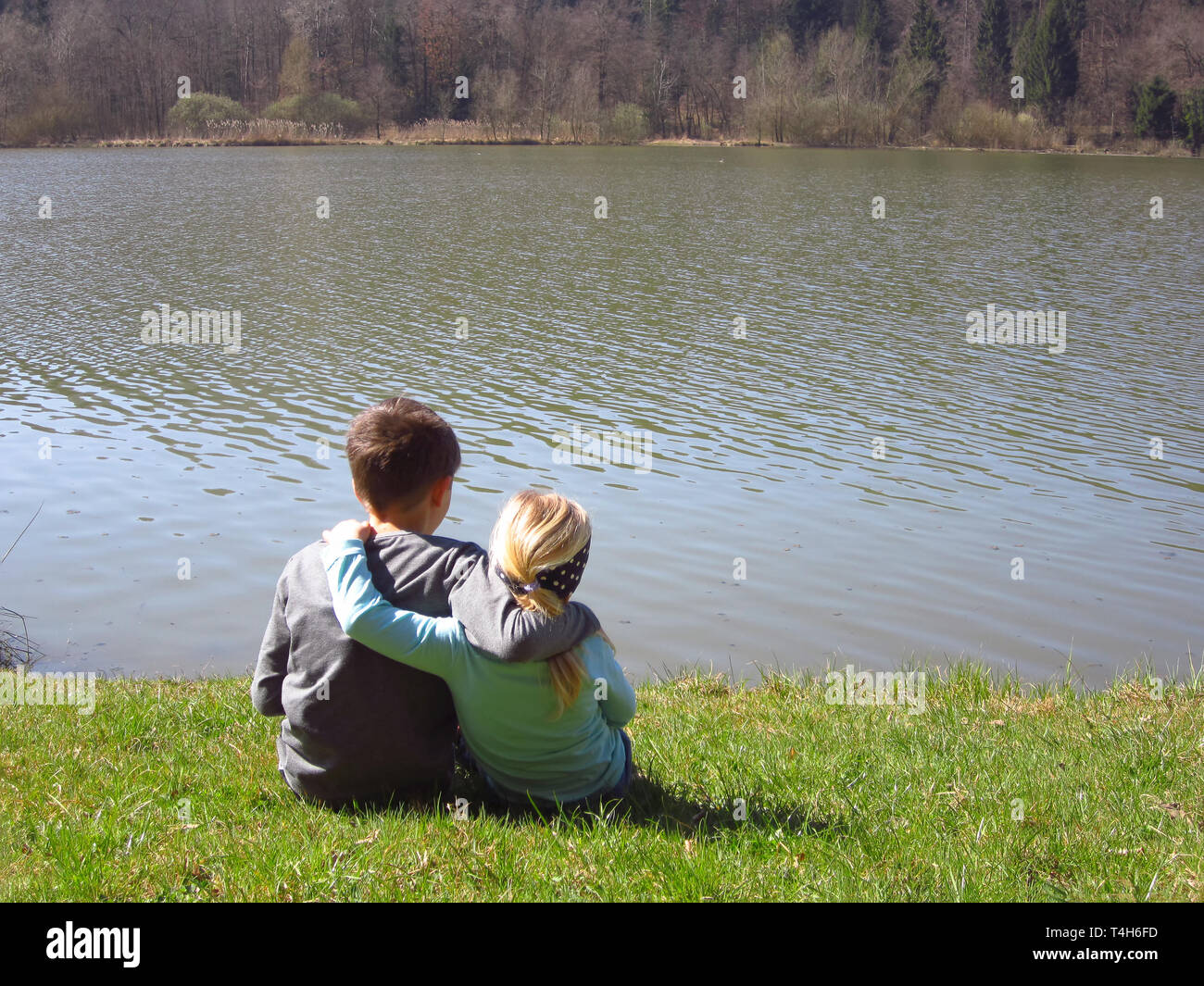 Little brother and sister by the lake hugging tight and beeing