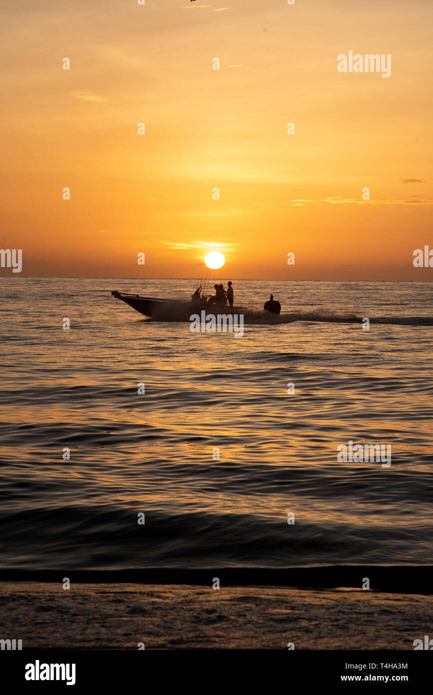 A boat passing through a golden, orange sunrise from the view from a beach. Stock Photo
